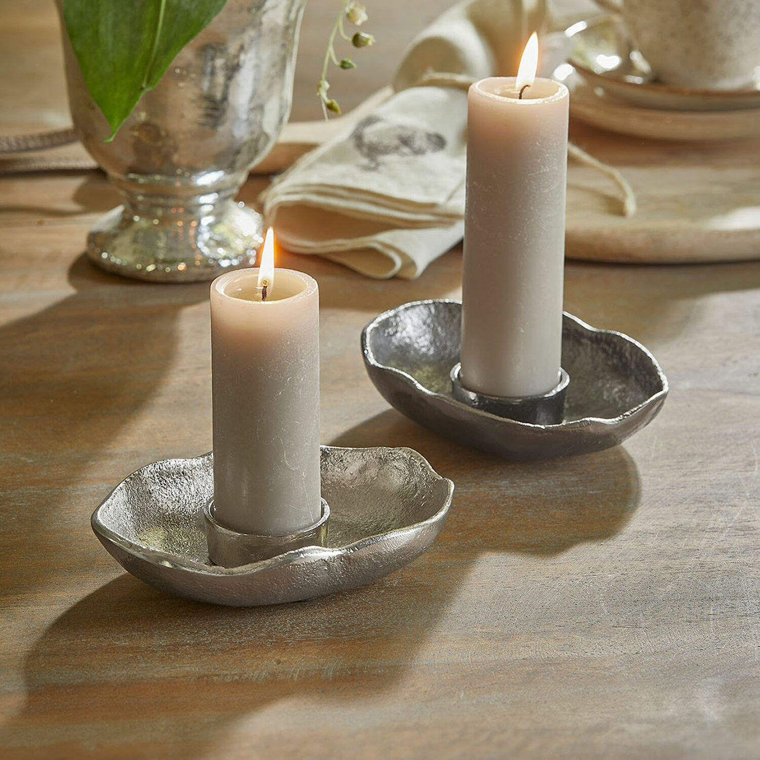 Kaarsenhouder set van 2 Quilvano Twee zilverkleurige metalen kandelaars met grijze kaarsen op houten tafel, interieurdecoratie