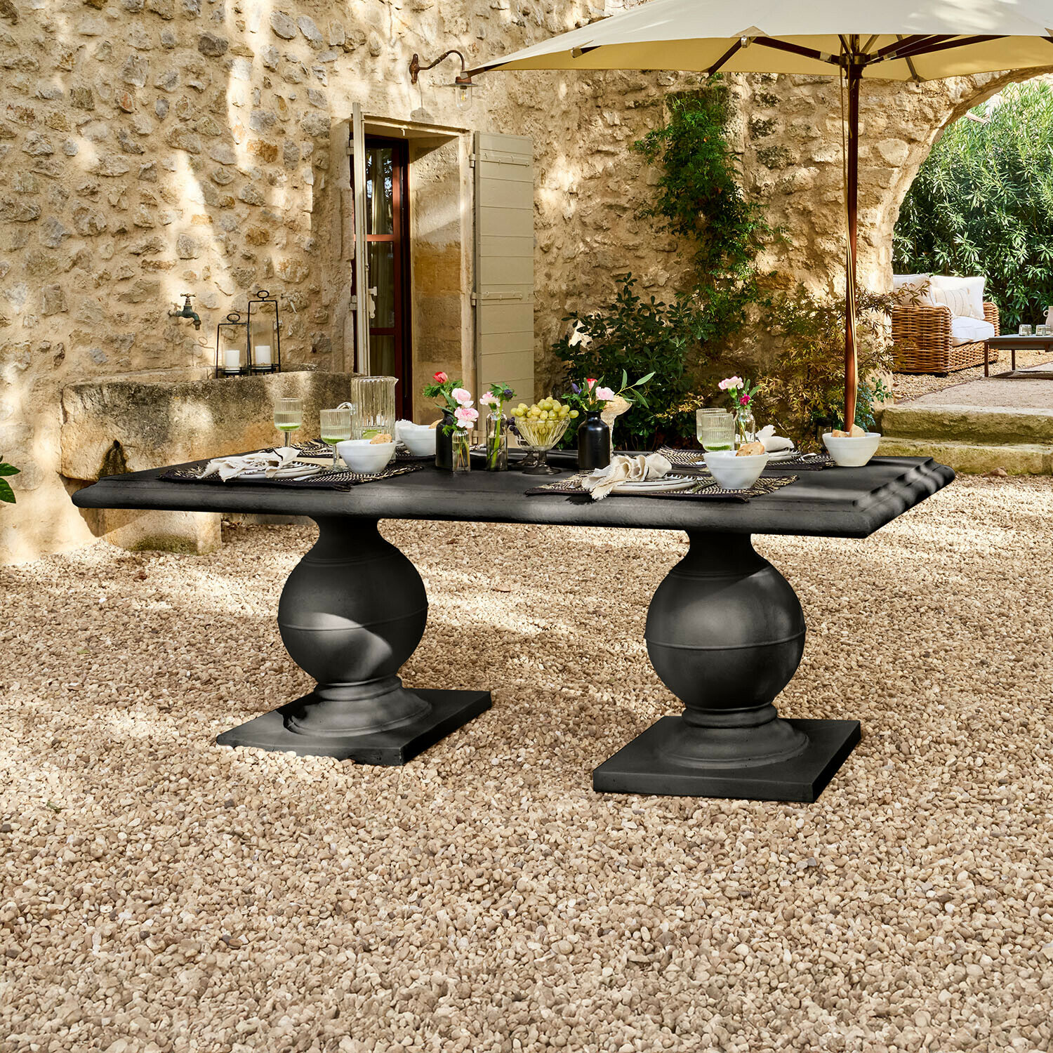 Zwarte stenen tuintafel met twee bolvormige poten op grindterras onder parasol
