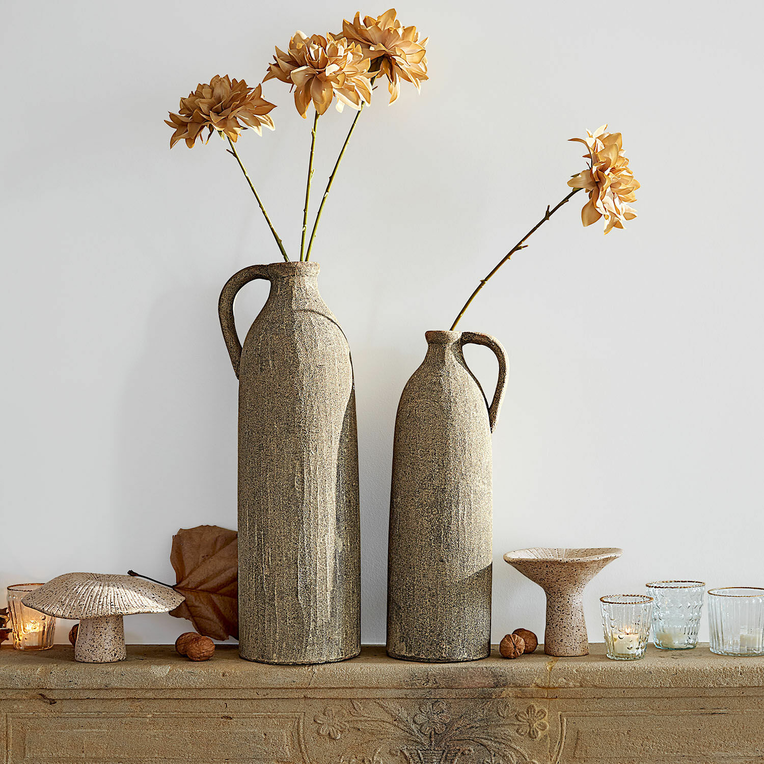 Twee hoge beige keramische vazen met gedroogde bloemen en decoraties op een stenen plank