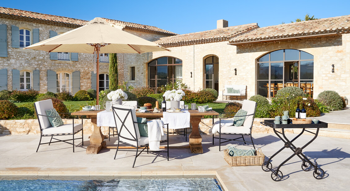 Tuinmeubelset met houten tafel en crèmekleurige kussens op terras bij zwembad