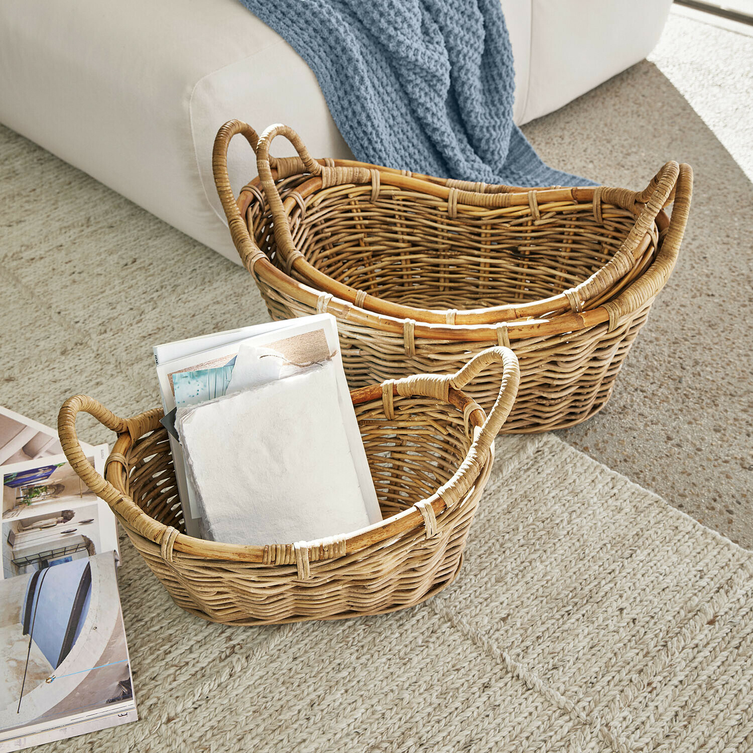 Twee natuurlijke rieten manden op tapijt, één gevuld met tijdschriften, praktische opbergmand