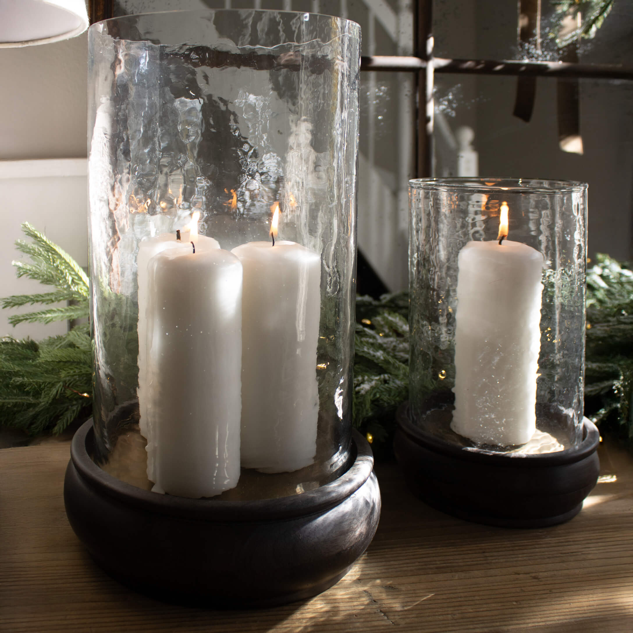 Glazen lantaarns met witte kaarsen op houten voet, kerstdecoratie met groene takken