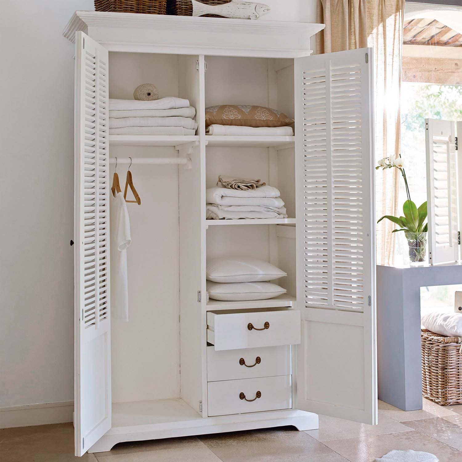 Witte houten kast met open deuren, opgevouwen witte textiel en kussens in lichte kamer