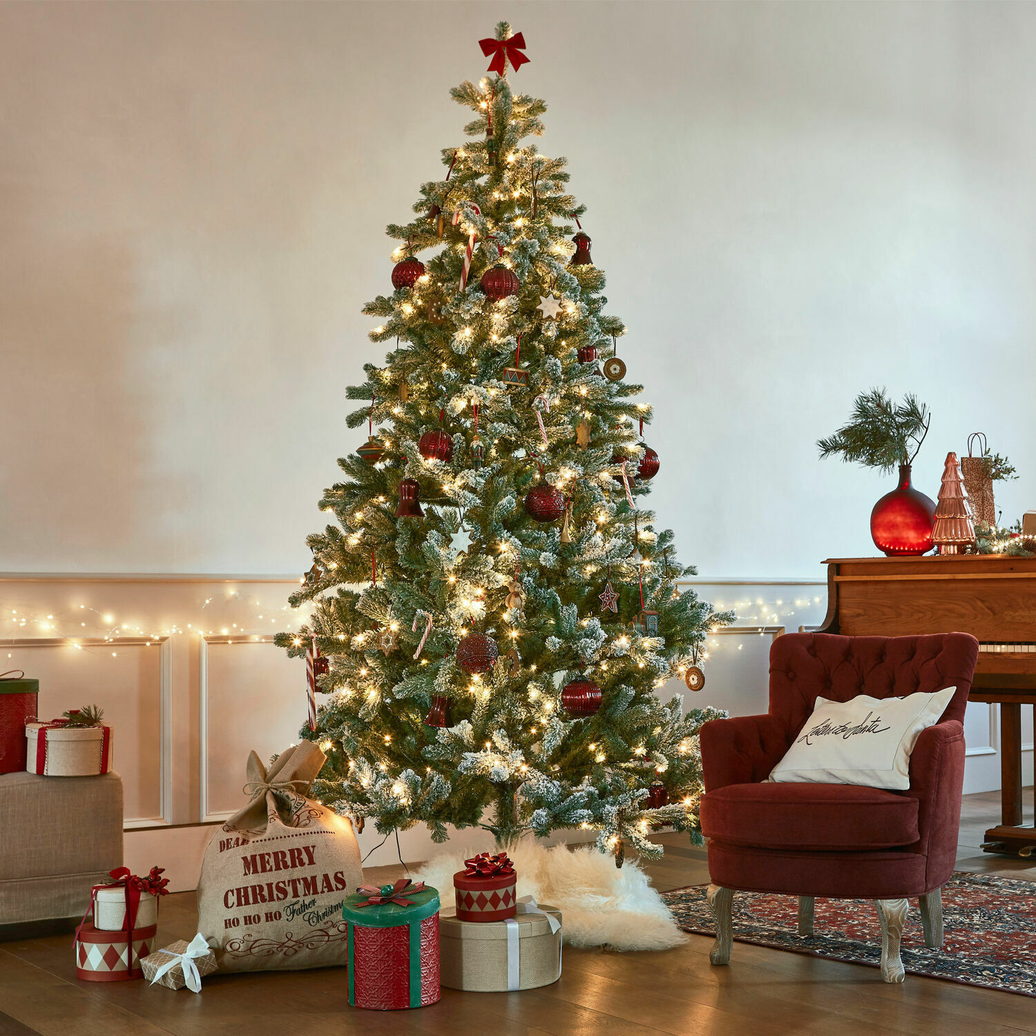 Kerstboom Mannier Kunstmatige besneeuwde kerstboom met rode versieringen en lichtjes in een gezellige woonkamer