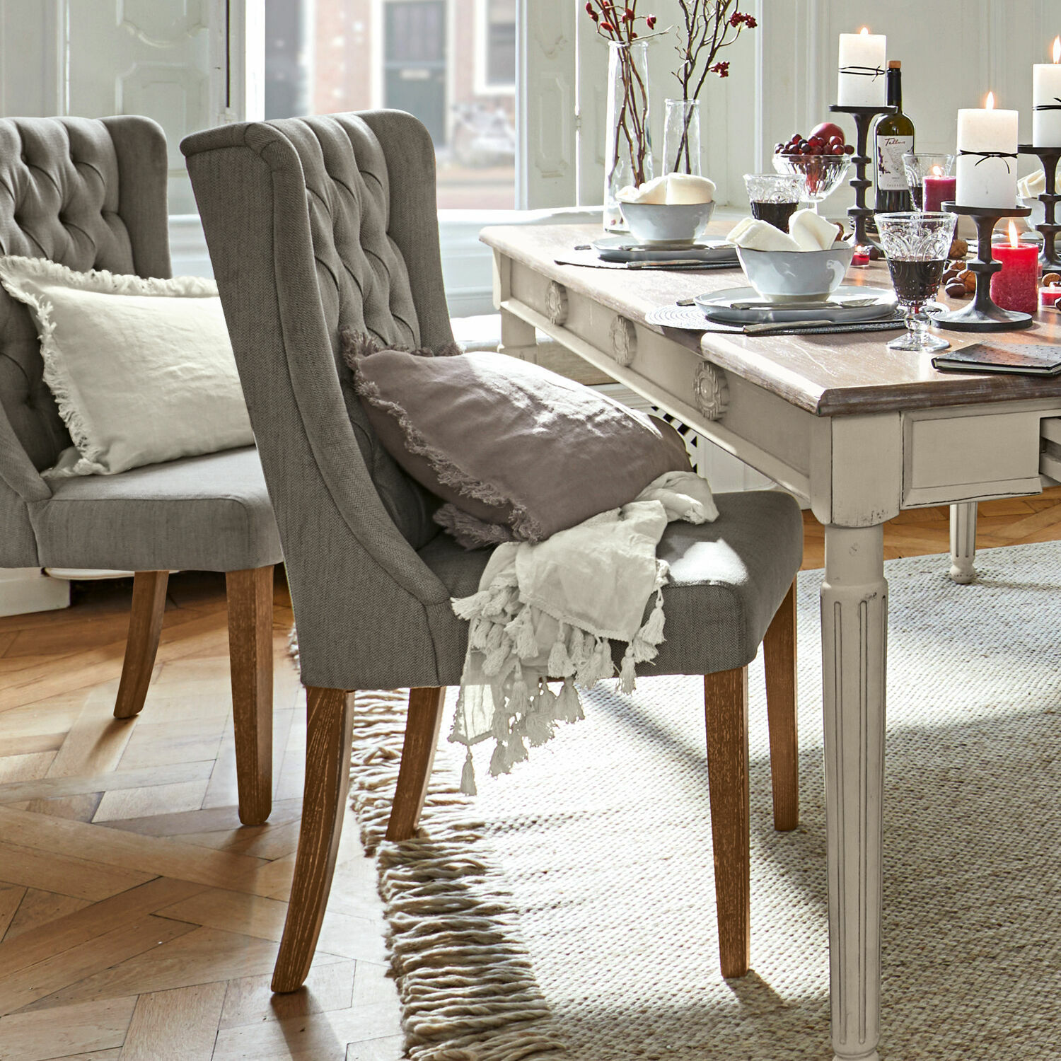 Grijze gestoffeerde stoel met houten poten bij lichte vintage tafel, decoraties op tafel