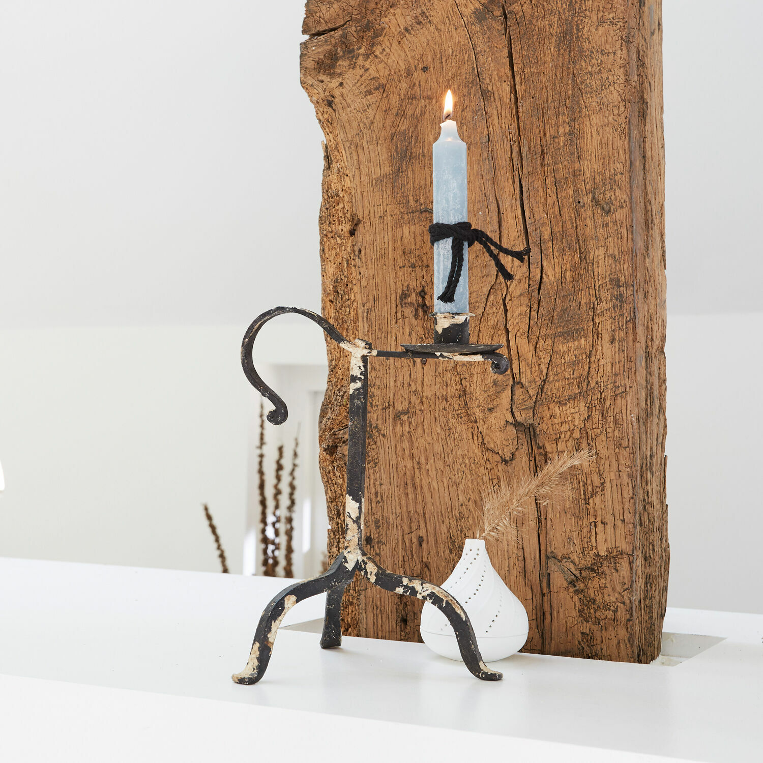 Metalen kandelaar met verweerde zwarte verf en blauwe kaars op witte en houten achtergrond