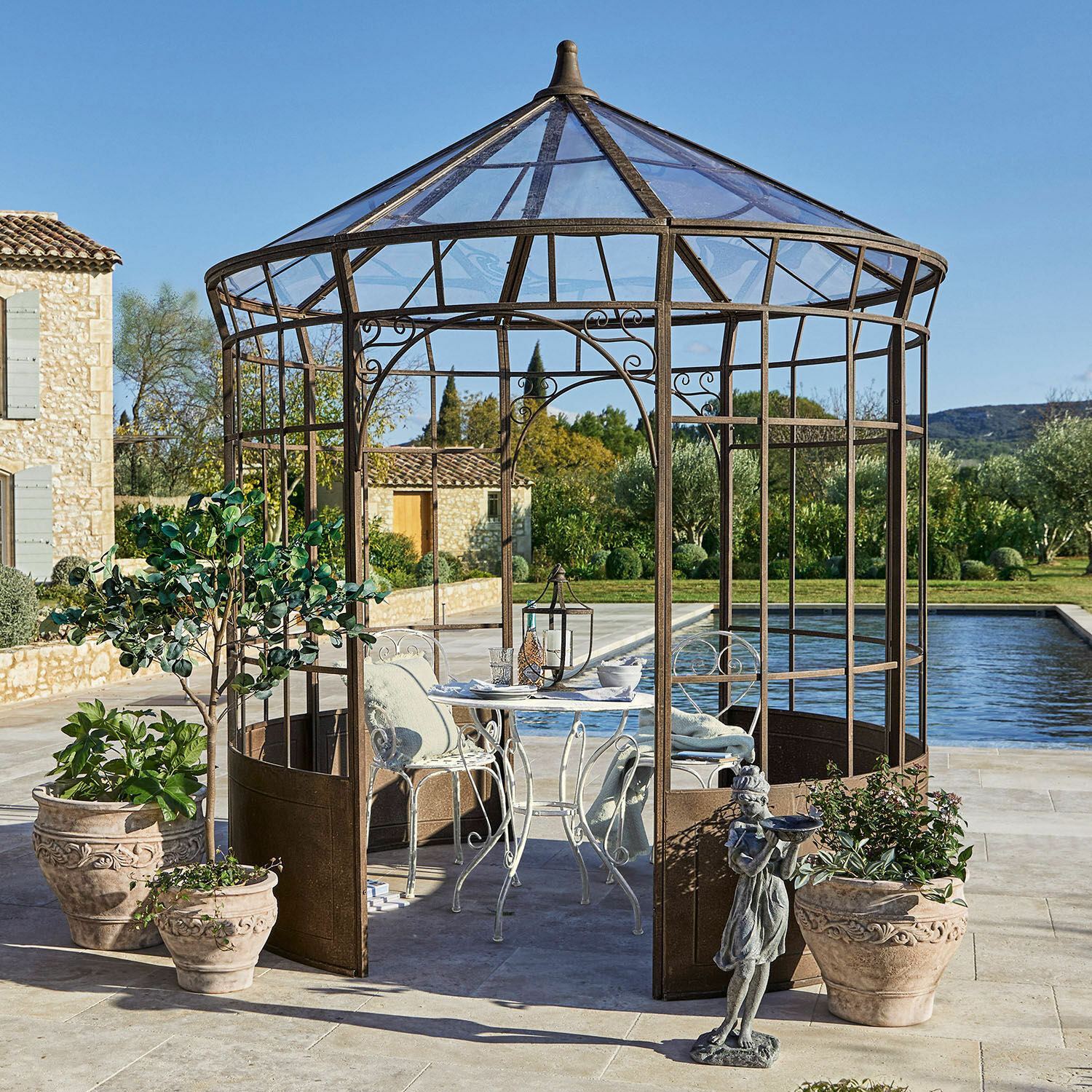 Paviljoen Murillo Decoratieve metalen tuinpaviljoen in roestkleur met witte tafel en stoelen op terras bij zwembad