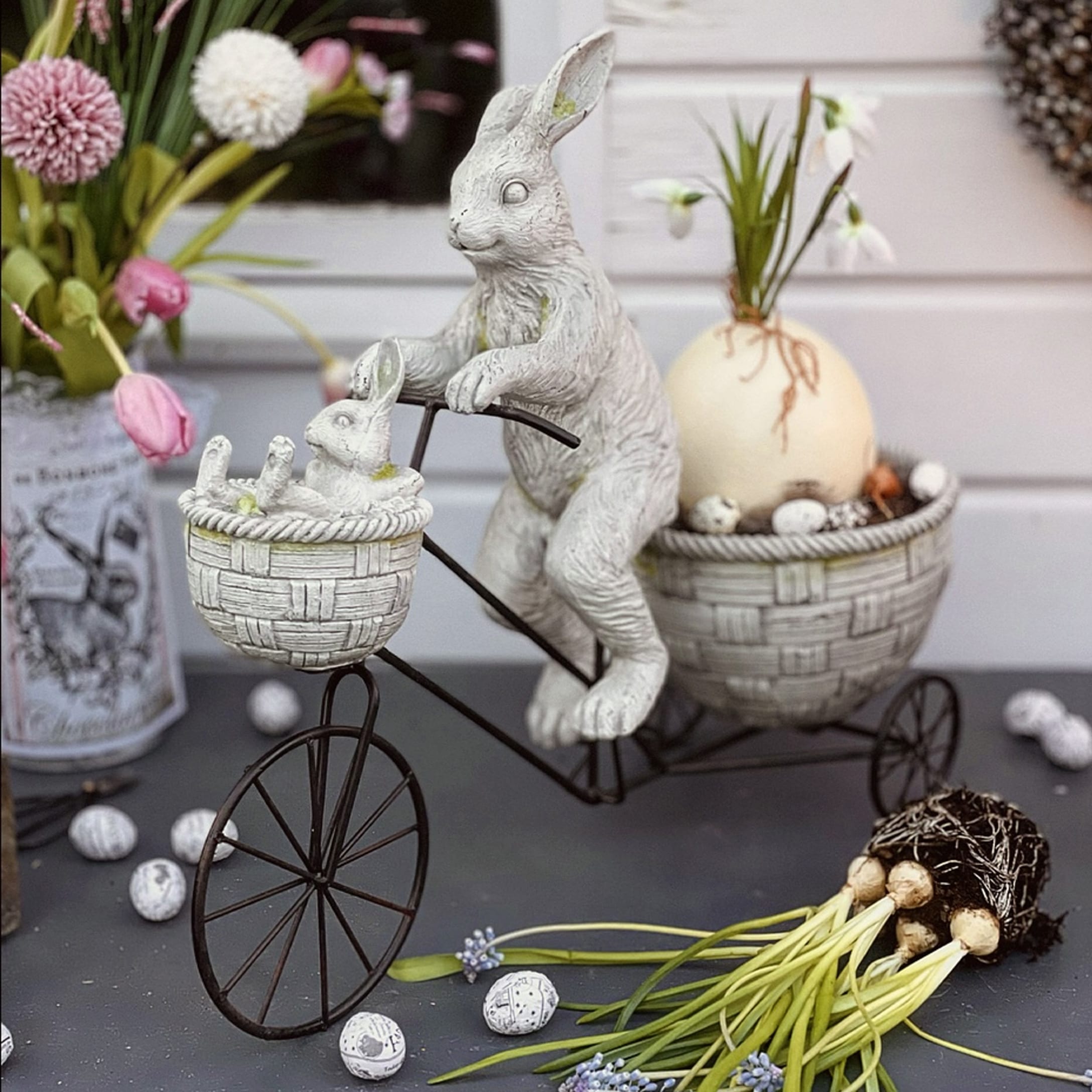 Paasdecoratie met witte kunststof konijnen op metalen fiets met manden en bloemen