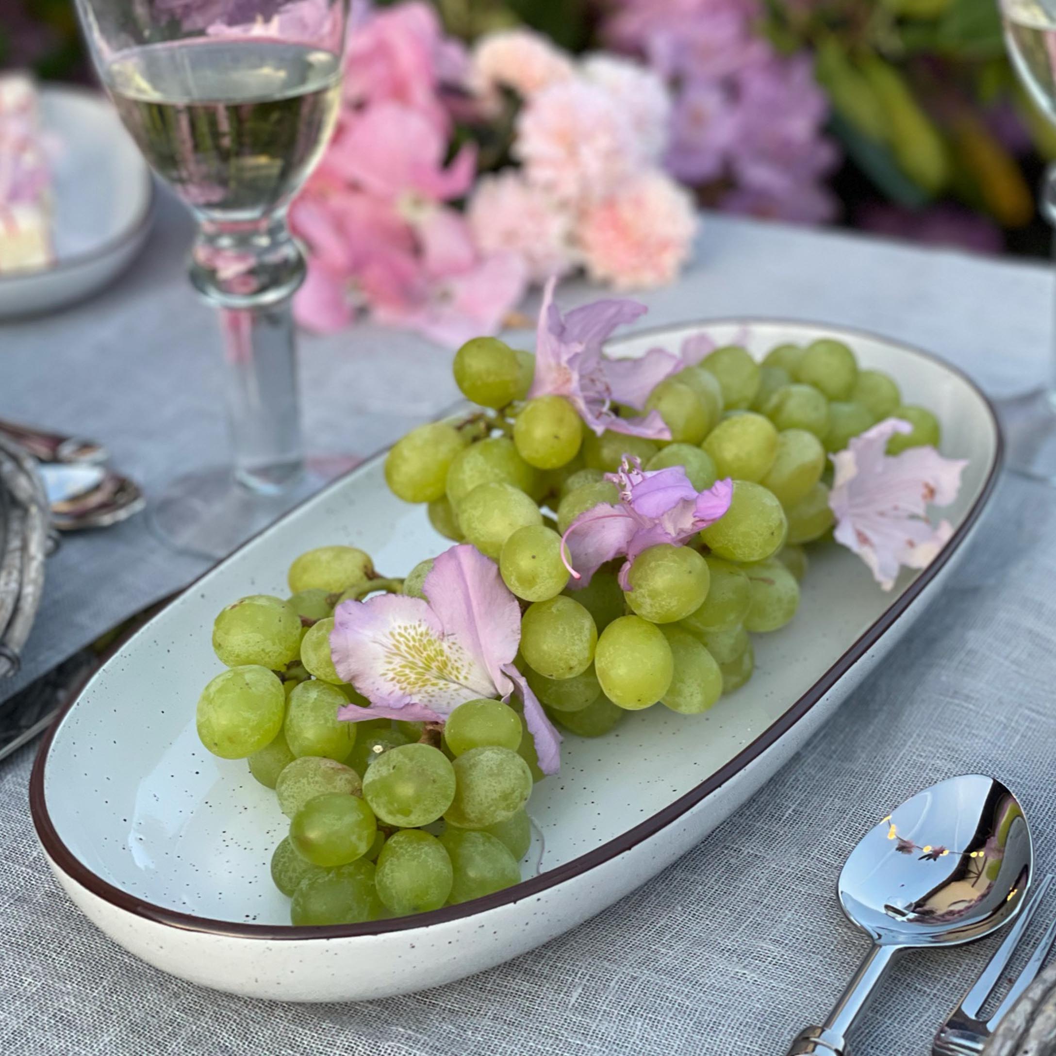 Groene druiven met roze bloemen op een wit keramisch bord op een grijs tafelkleed