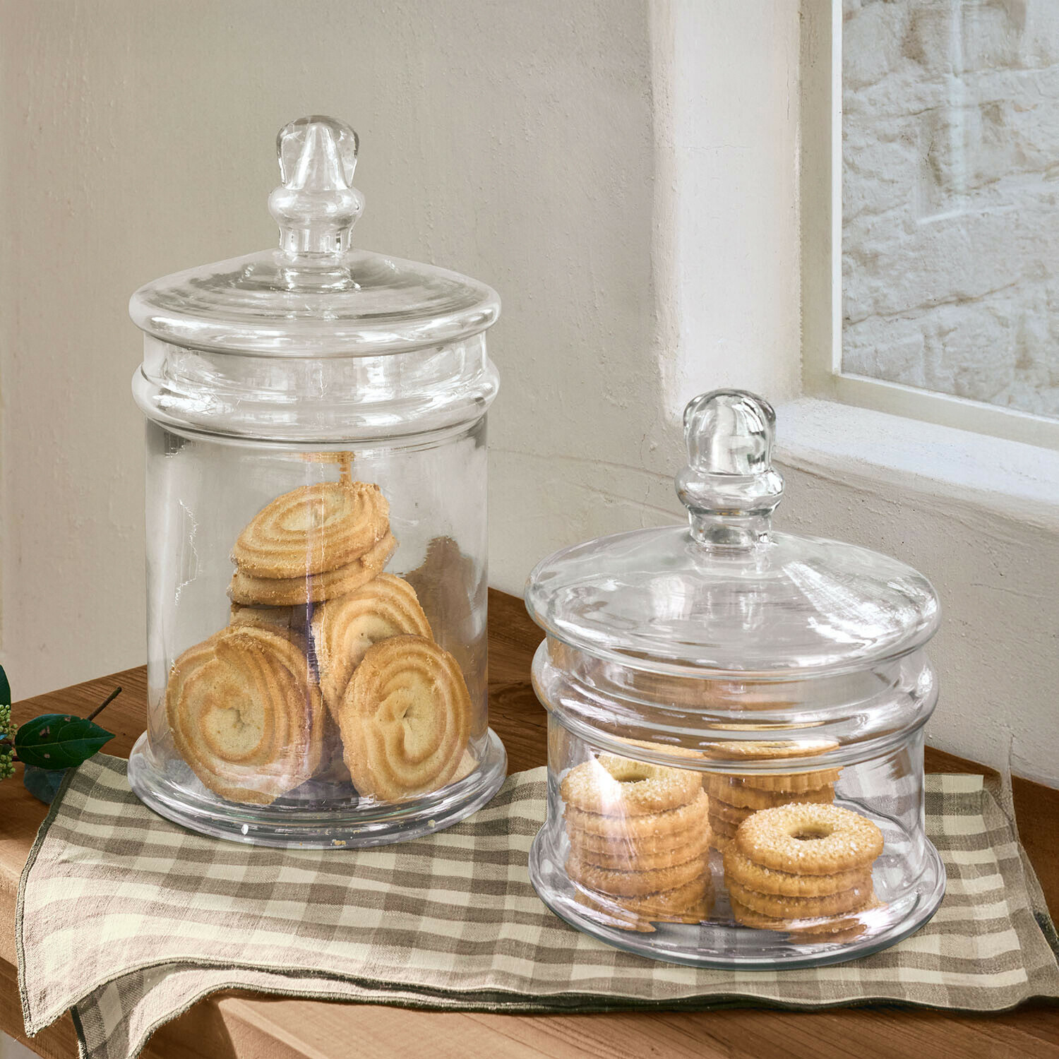 Pot set van 2 Quélaron Twee doorzichtige glazen potten met deksels gevuld met koekjes op een houten tafel met geruit kleed
