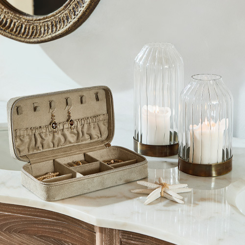 Beige sieradendoos met vakjes en oorbelhaken op marmeren blad met decoratieve kaarsen