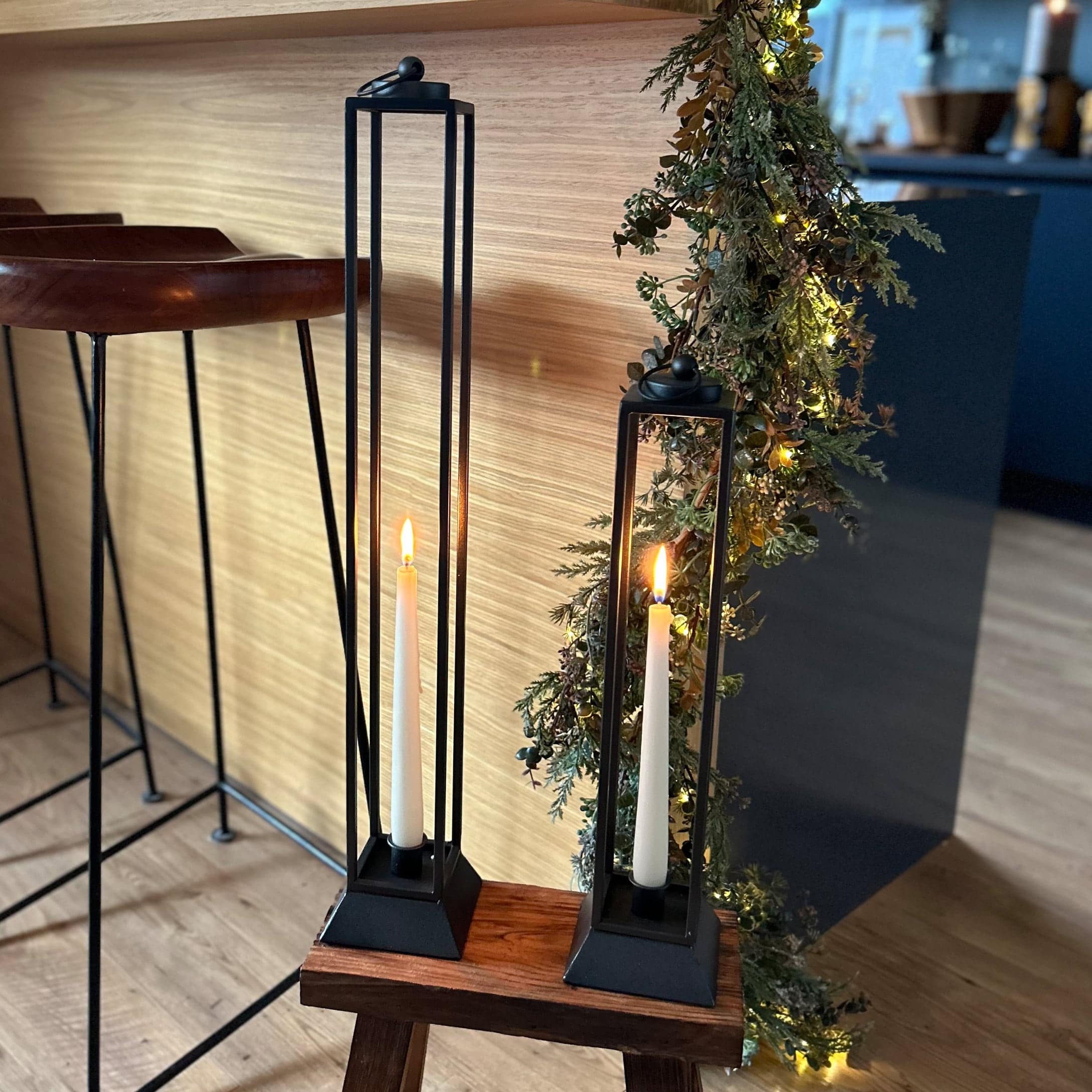 Twee zwarte metalen kandelaren met witte kaarsen op een houten kruk in een modern interieur