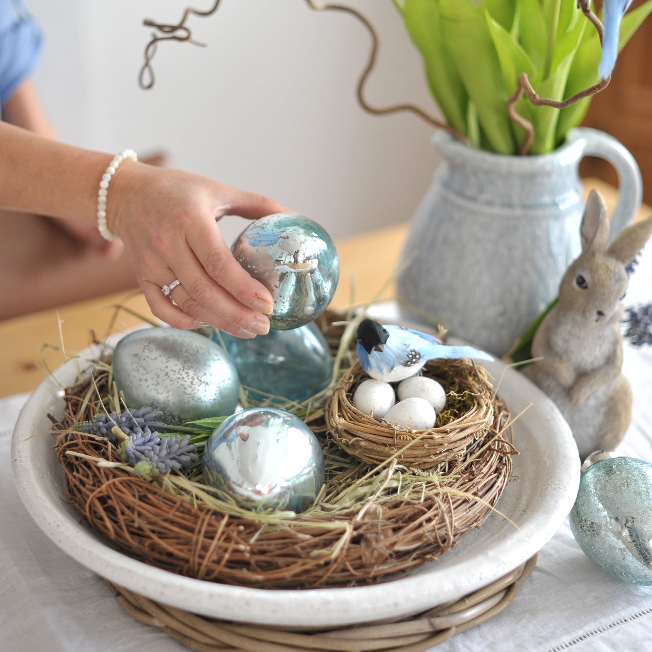 Paasdecoratie met blauwe glazen eieren en nest met witte eieren op houten tafel