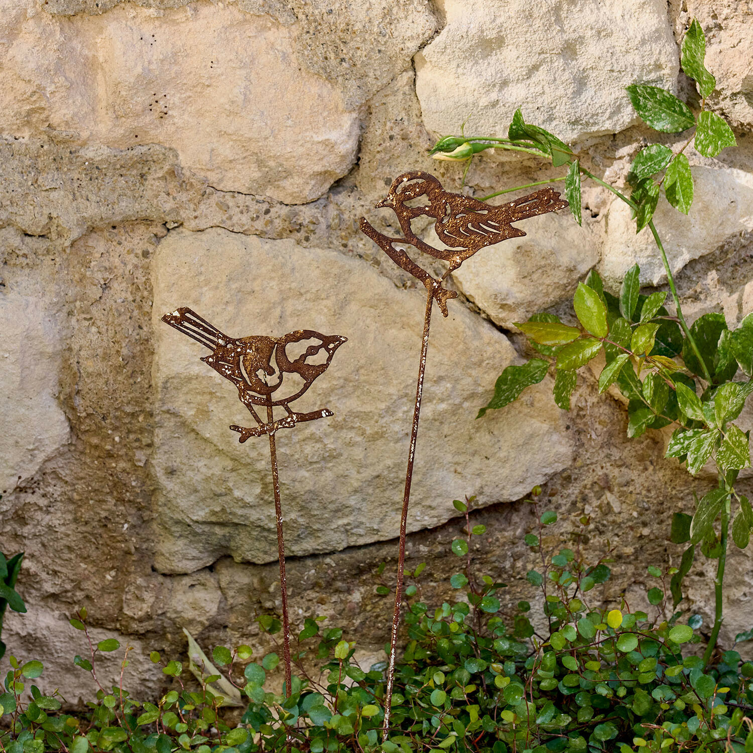 Tuinsteker set van 2 Pelvaron Decoratieve metalen vogels met roestkleurige afwerking op stokken in de tuin bij een stenen muur