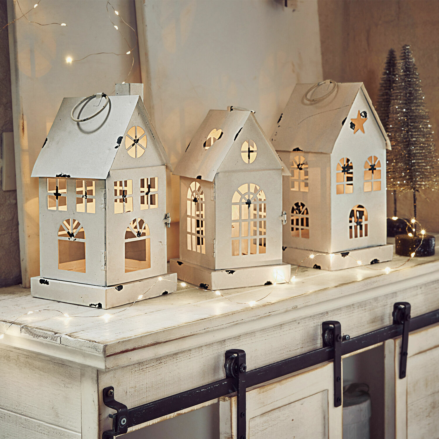 Set van drie witte metalen lantaarns in huisvorm met uitgesneden ramen en feestelijke verlichting