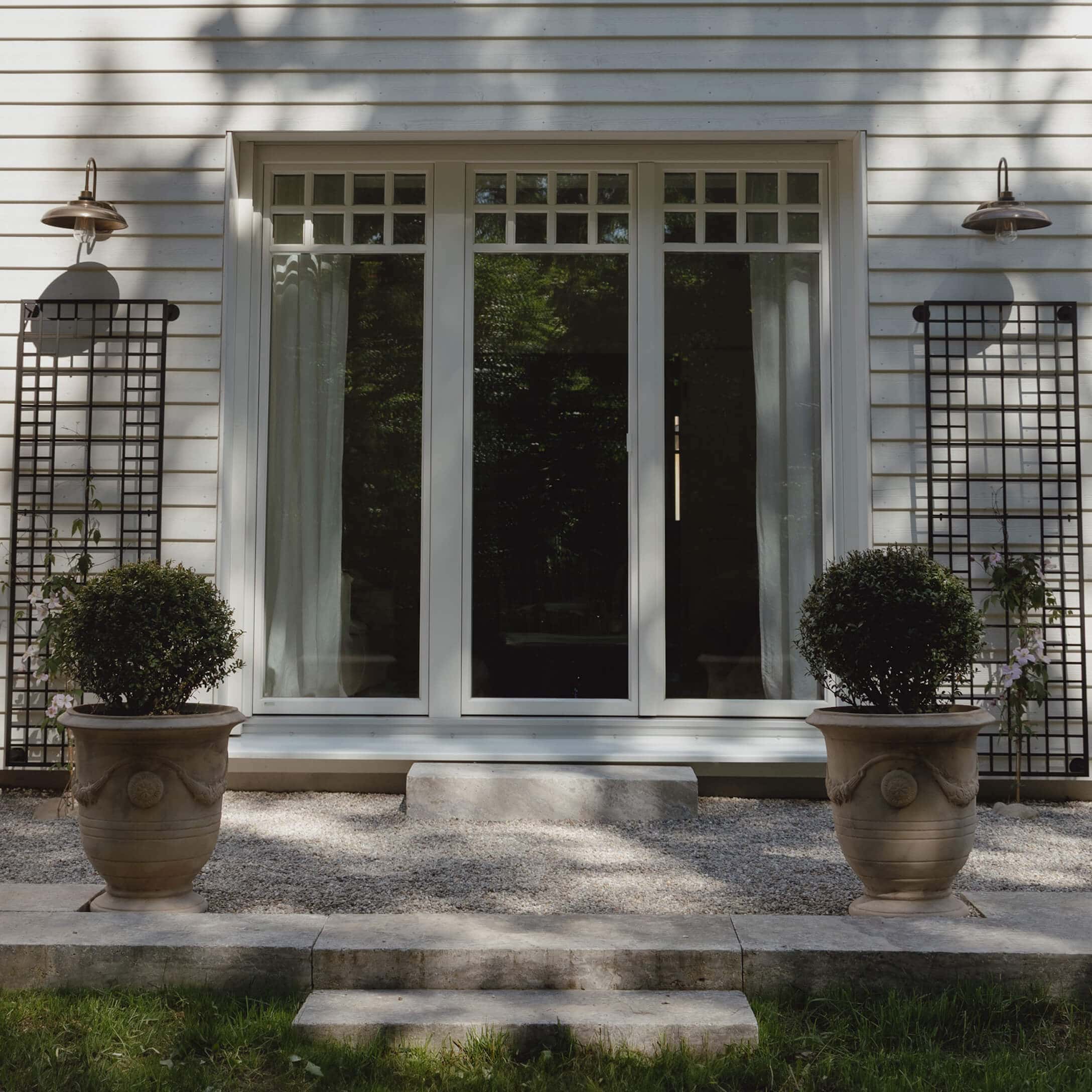 Huisentree met witte deur en twee grote stenen potten met groene planten op grind