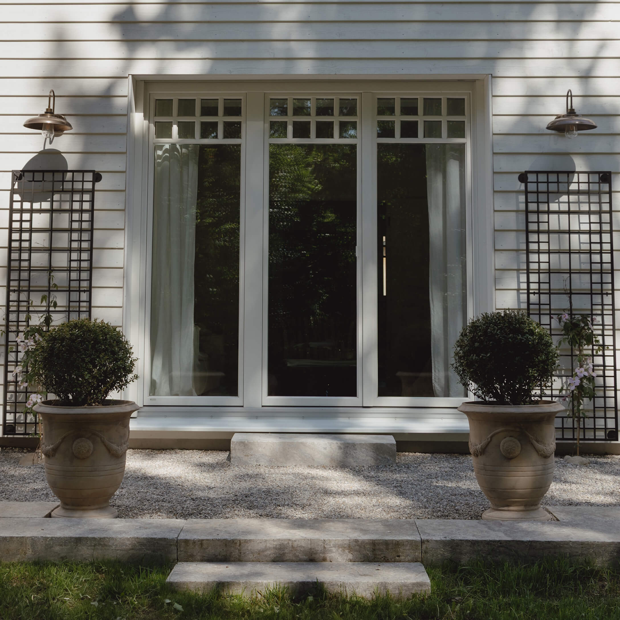 Huisentree met witte deur en twee grote stenen potten met groene planten op grind