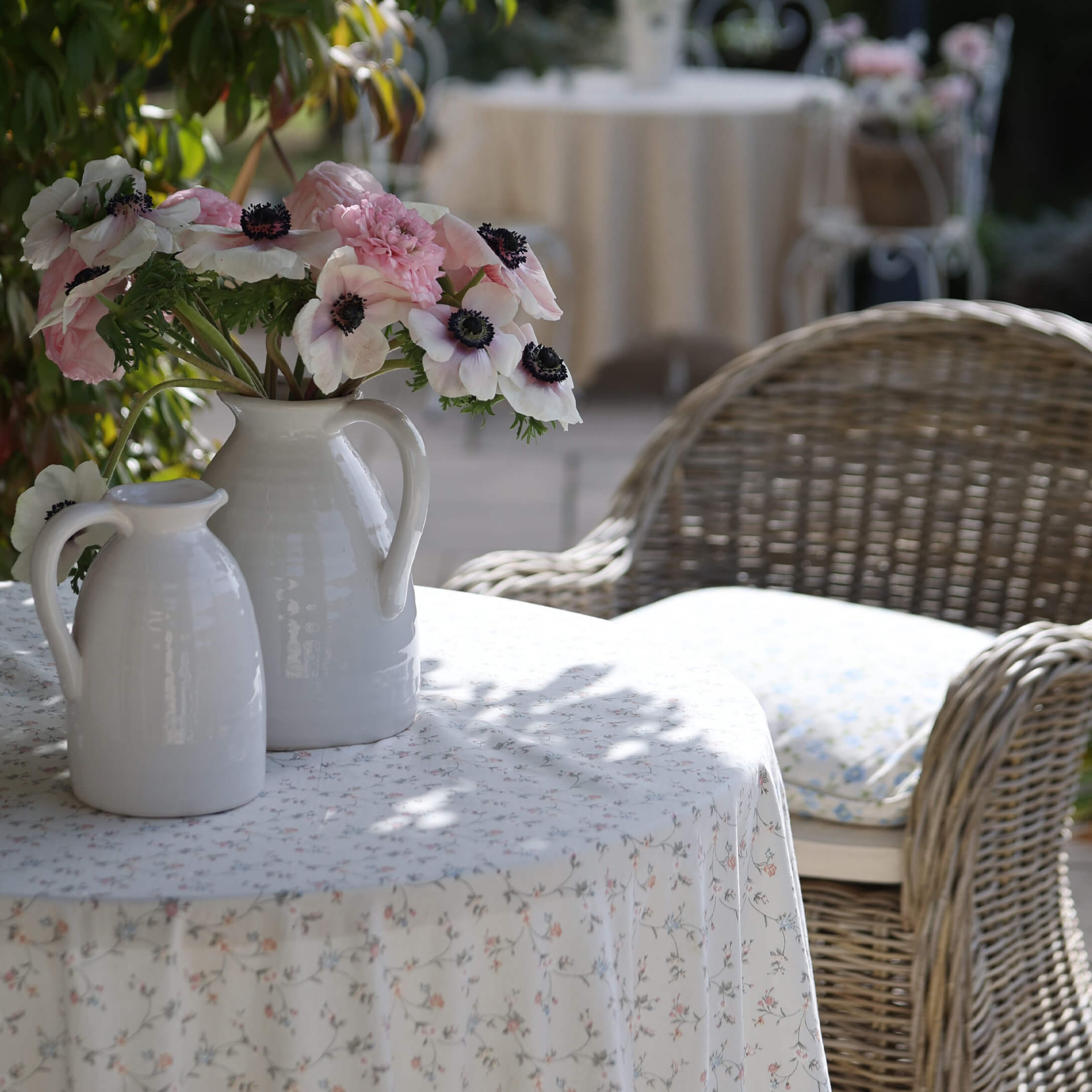 Witte keramische kannen met roze en witte bloemen op een tafel met bloemen tafelkleed in de tuin