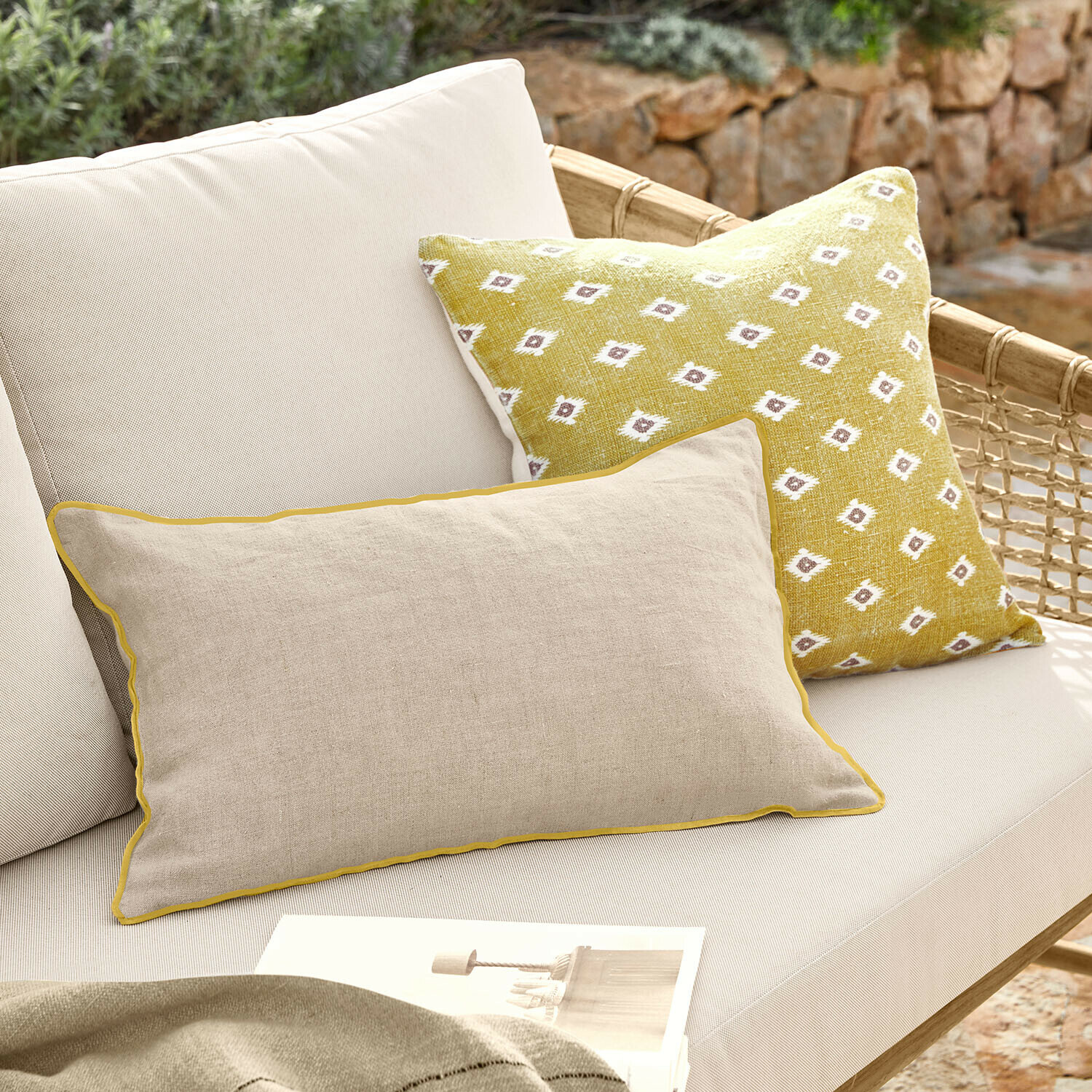 Beige linnen kussen met gele bies en geel kussen met wit patroon op lichte loungesofa buiten