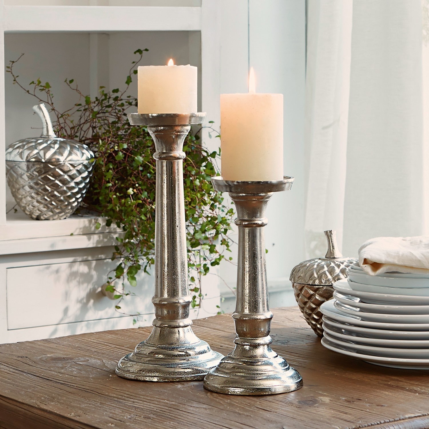 Kandelaar set van 2 Symone Twee zilverkleurige metalen kandelaars met witte kaarsen op houten tafel voor interieurdecoratie