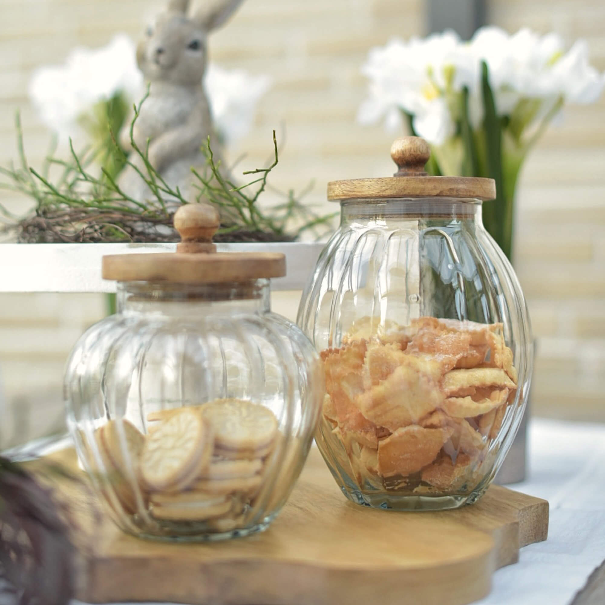 Glazen potten met houten deksels gevuld met koekjes op houten plank, paasdecoratie