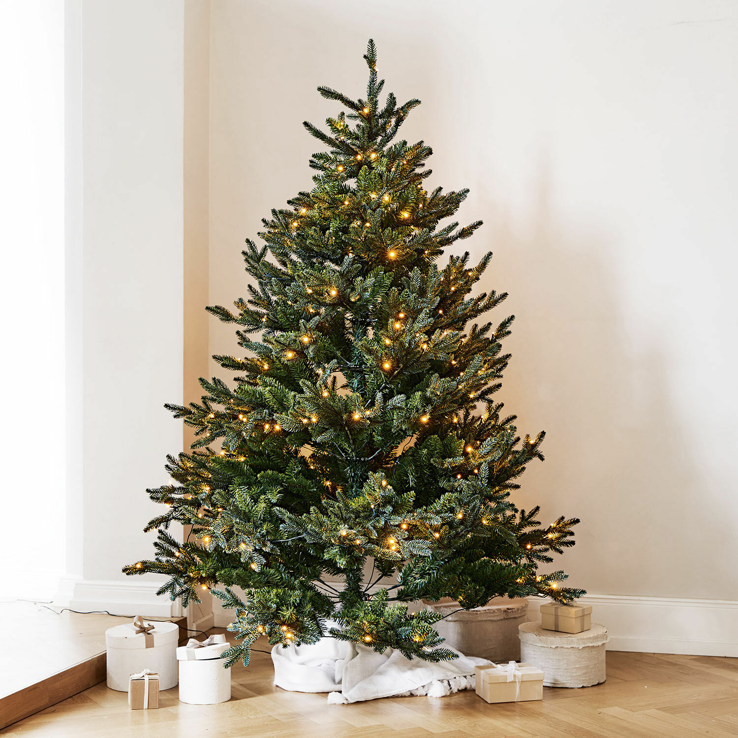 Kunstkerstboom met groene naalden en warme LED-verlichting op houten vloer met cadeaus