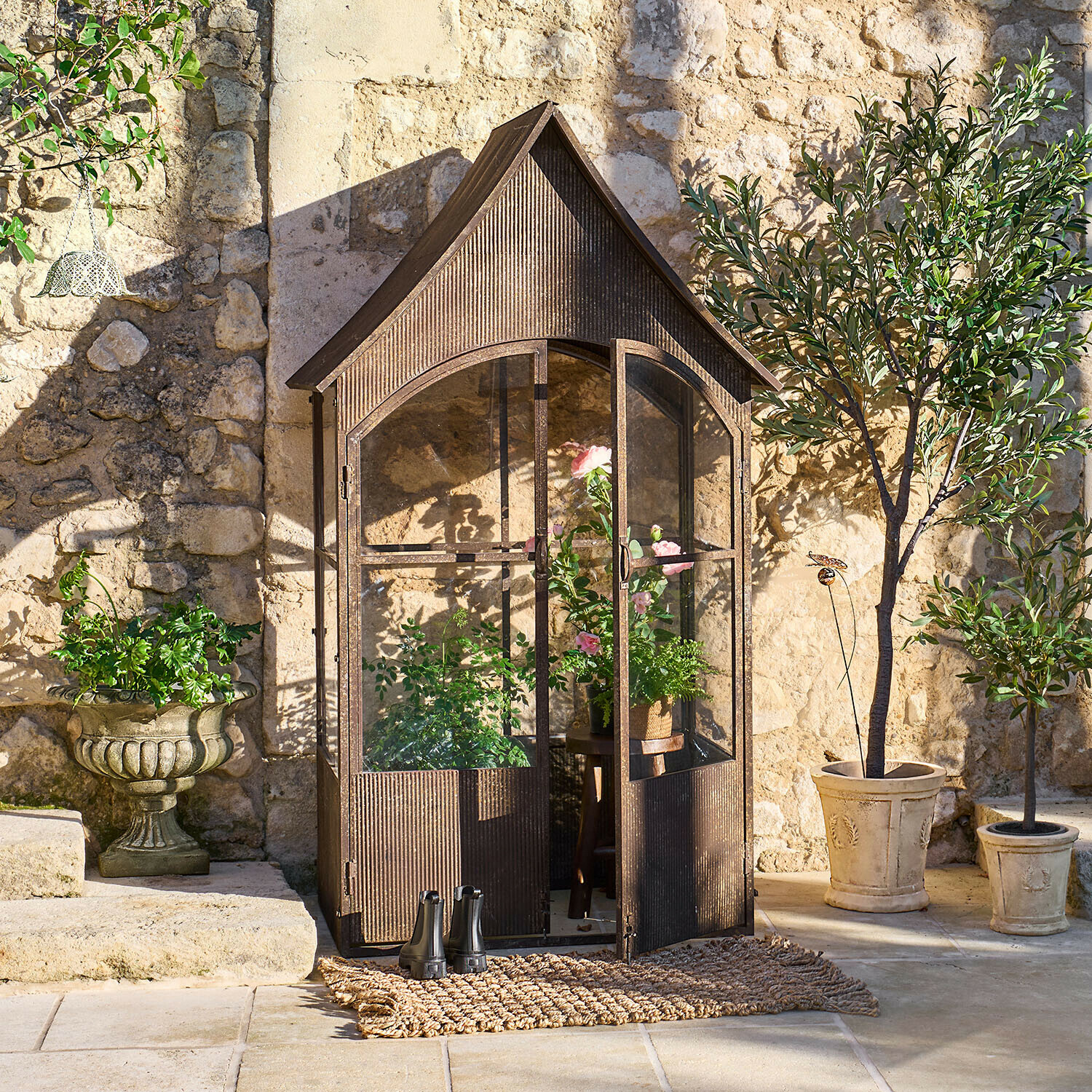Vintage metalen broeikas in bruine kleur met planten en potten voor een zonnige stenen muur in de tuin