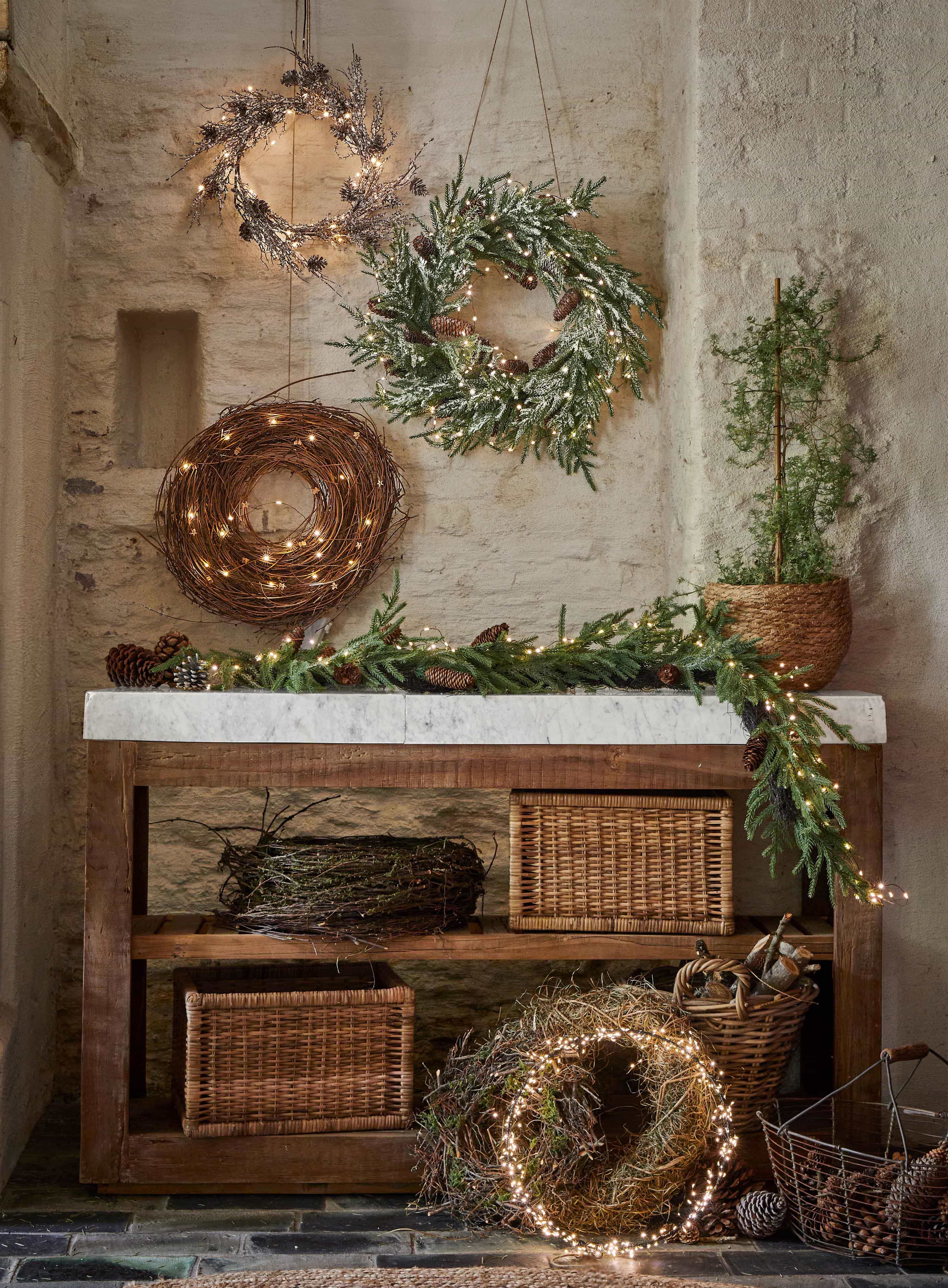 Decoratieve kerstkransen van takken, dennenappels en lichtjes op houten tafel in rustieke ruimte