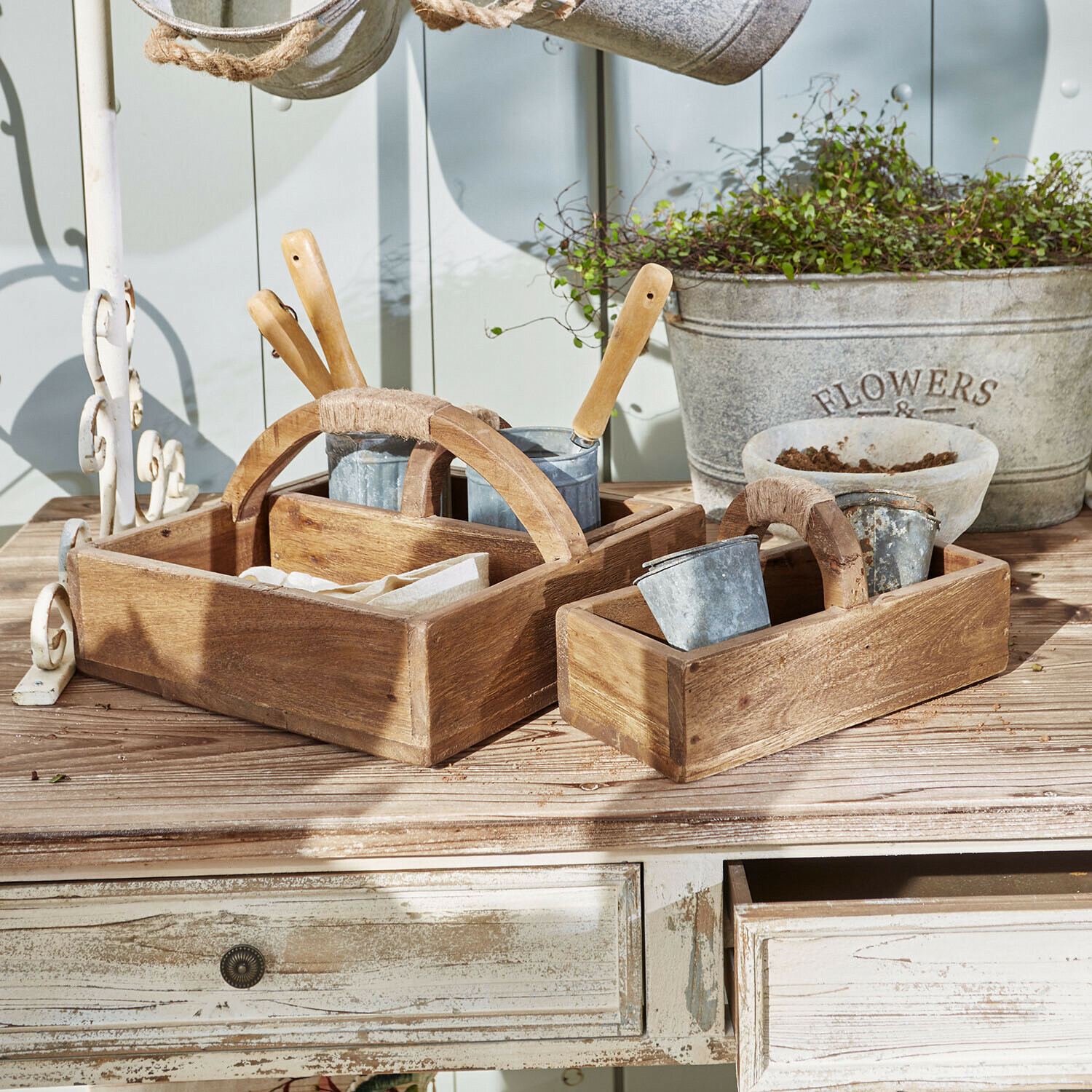 Houten bakken met handvatten en metalen potten op tuintafel voor tuingereedschap en planten