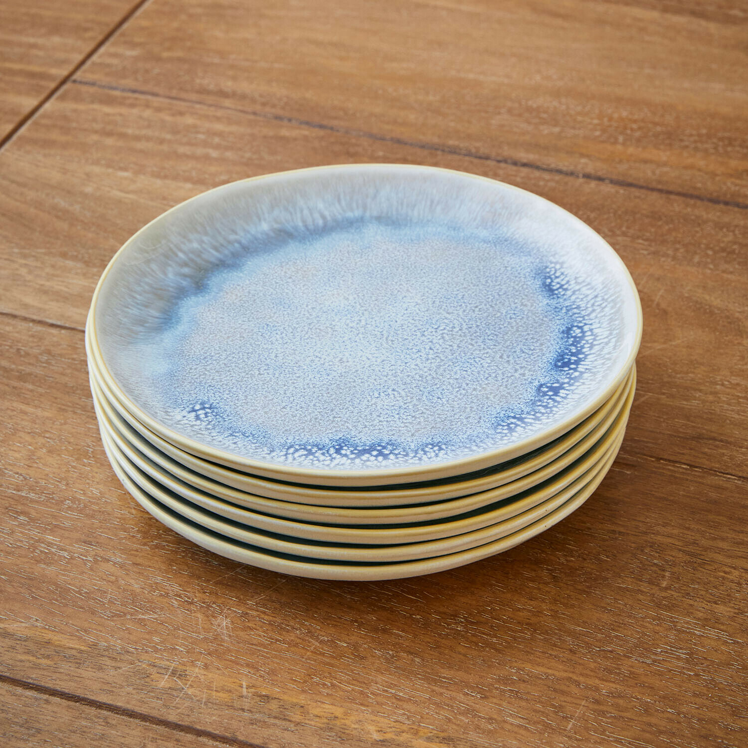 Set van zes keramische borden in blauw en crème op een houten tafel gestapeld