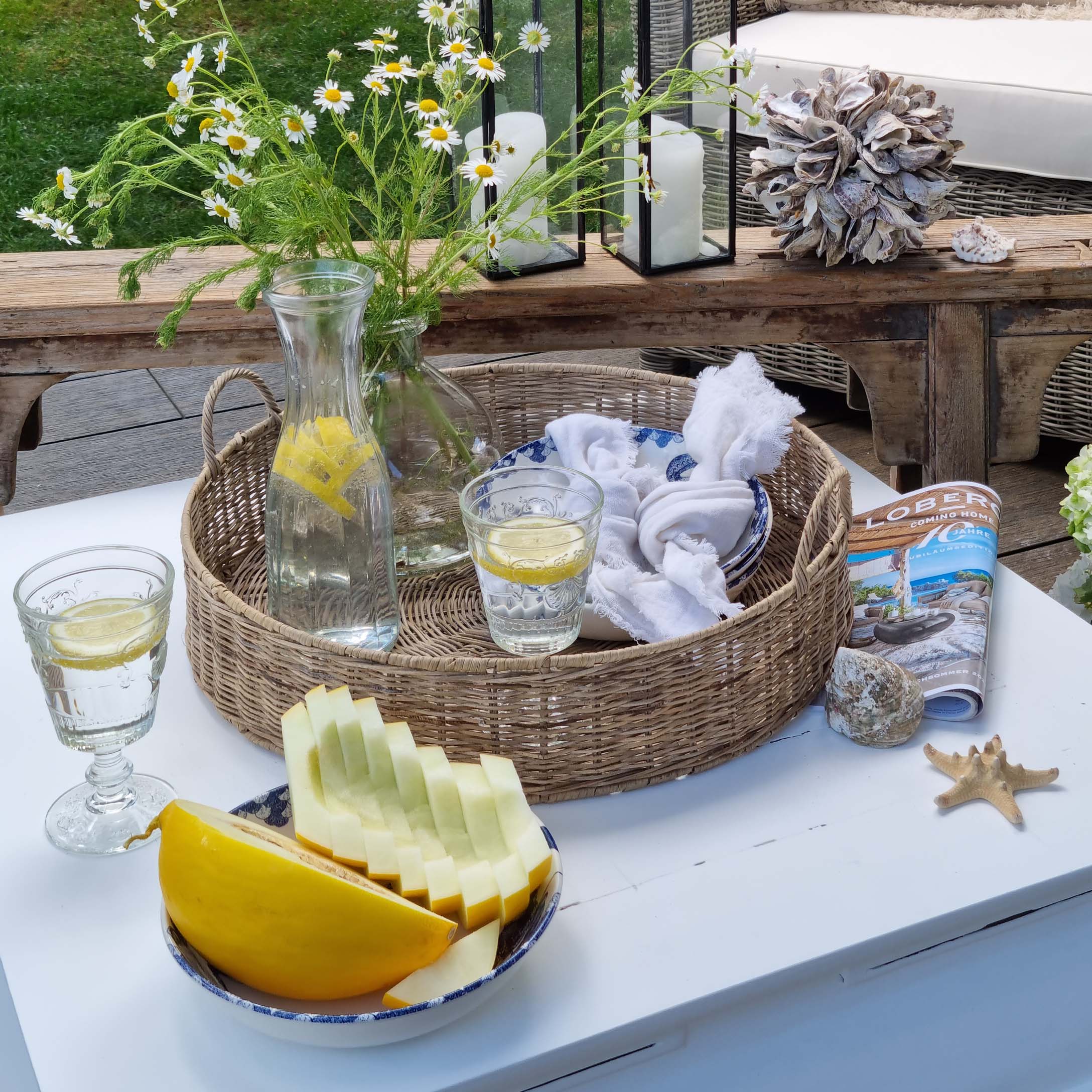 Ronde rieten mand met karaf citroenwater en glas op witte tafel in tuin