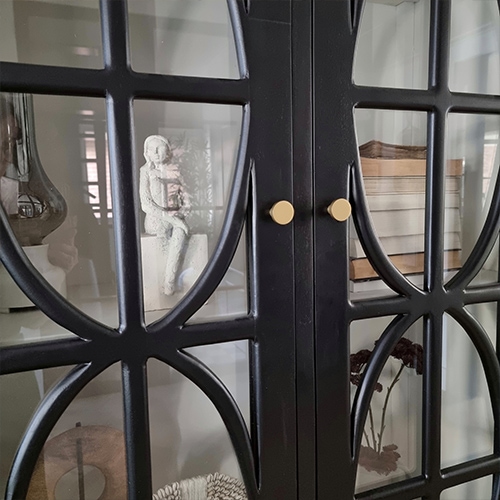 Zwarte metalen kast met decoratief patroon en glazen deuren, decoraties zichtbaar binnenin