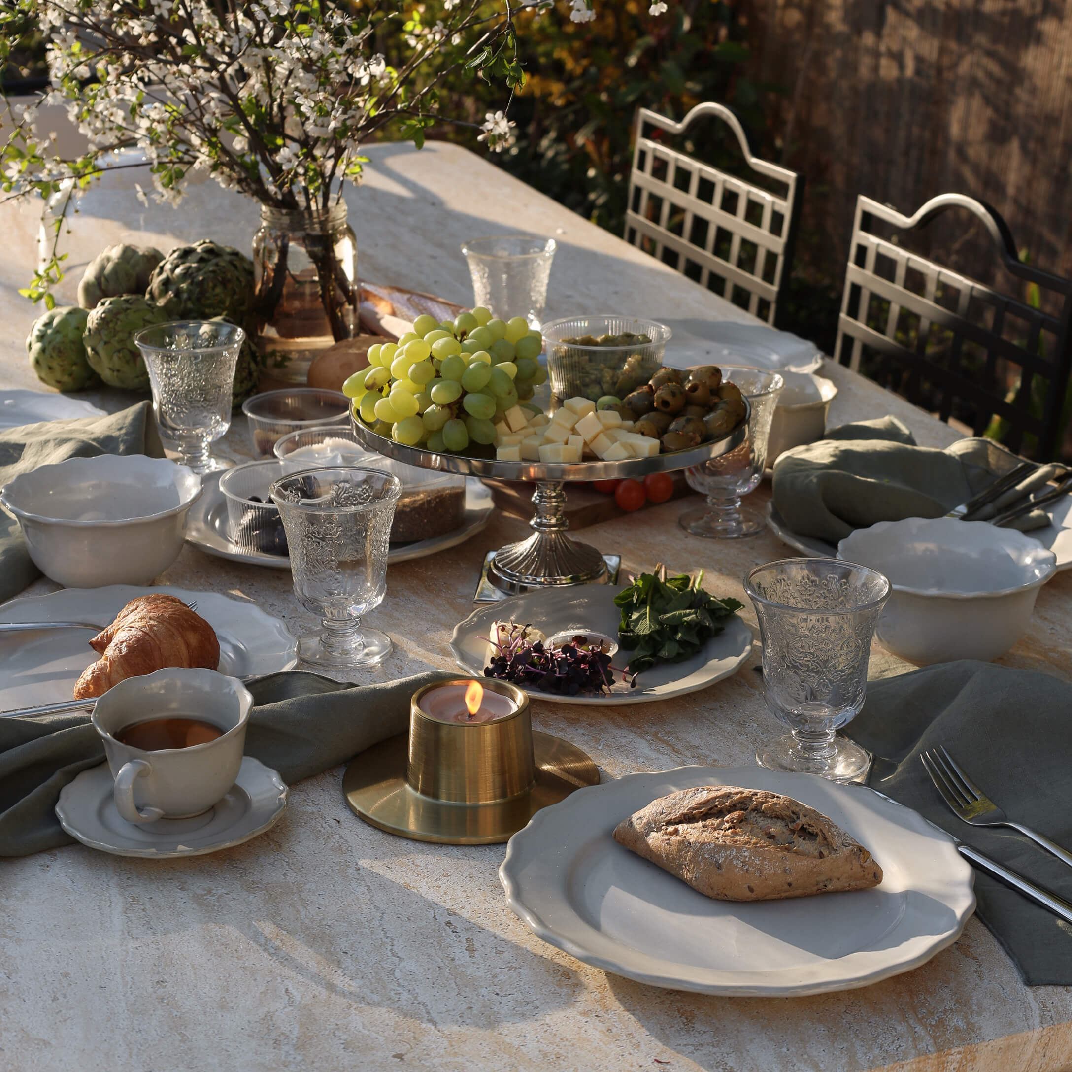 Steentafel met wit servies, kaars en schaal met druiven, kaas en olijven buiten
