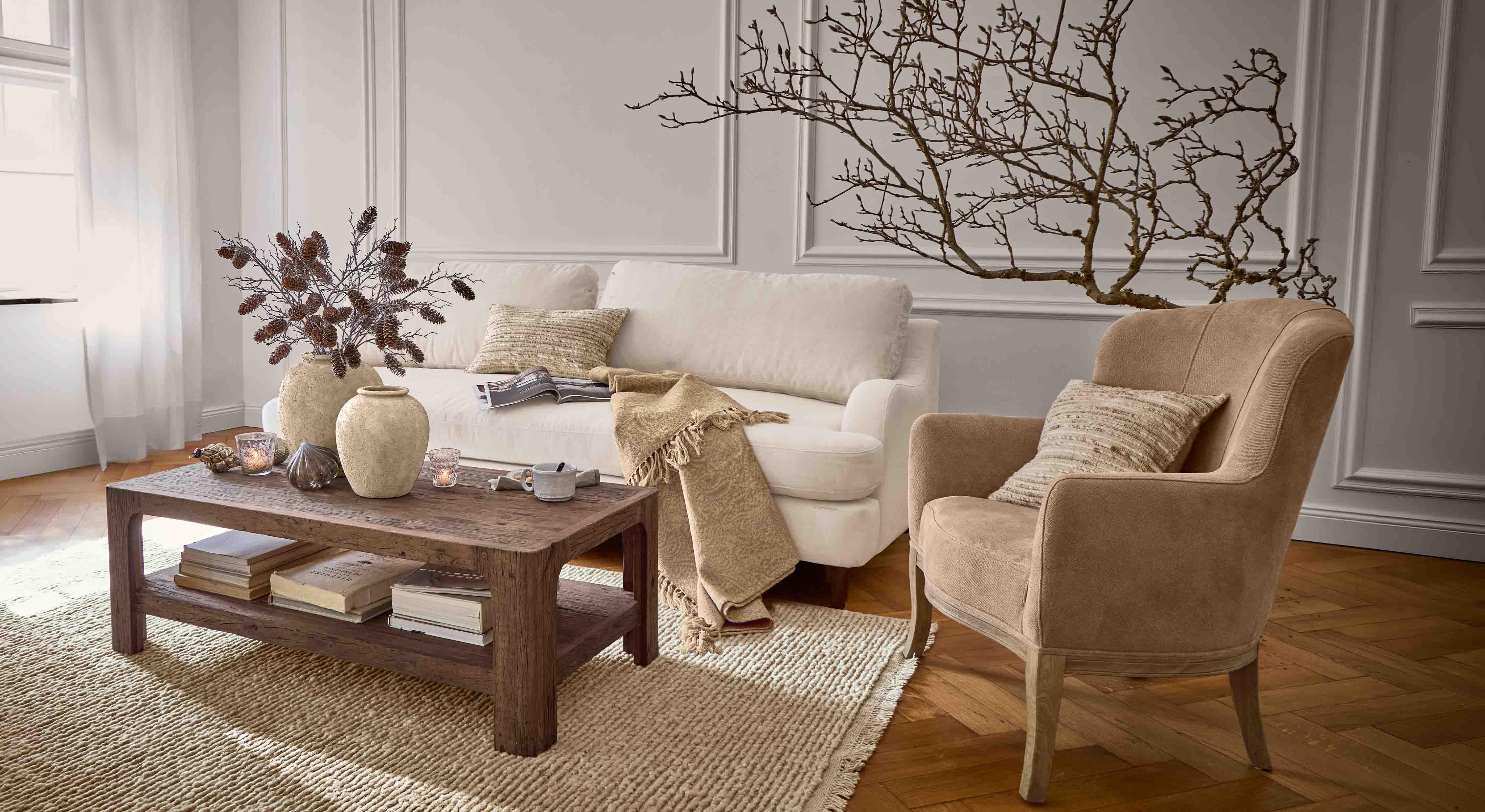 Gezellige woonkamer met beige bank, bruine fauteuil en houten salontafel op geweven vloerkleed