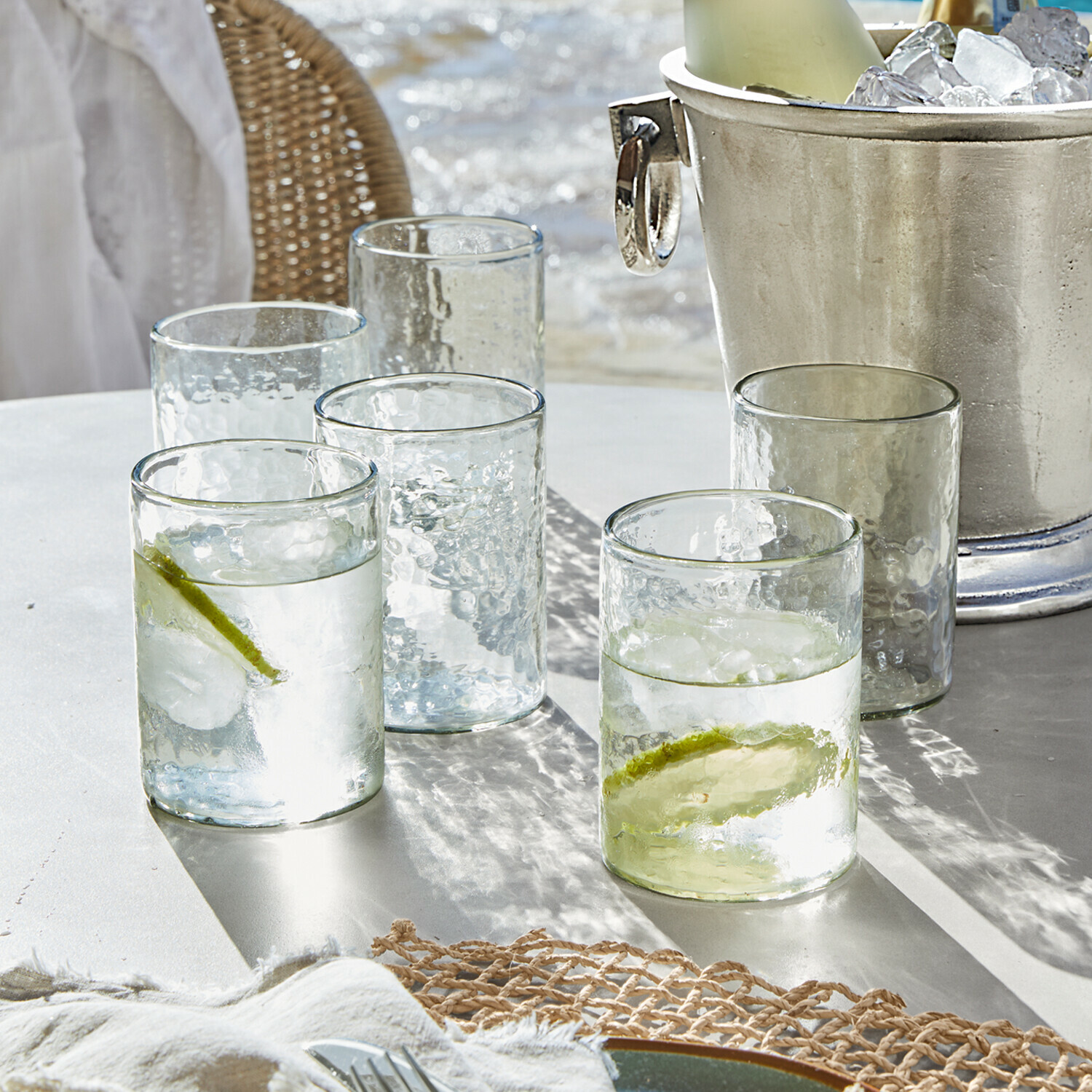 Glazen van doorzichtig, gestructureerd glas met limoenpartjes en ijsblokjes op witte tafel