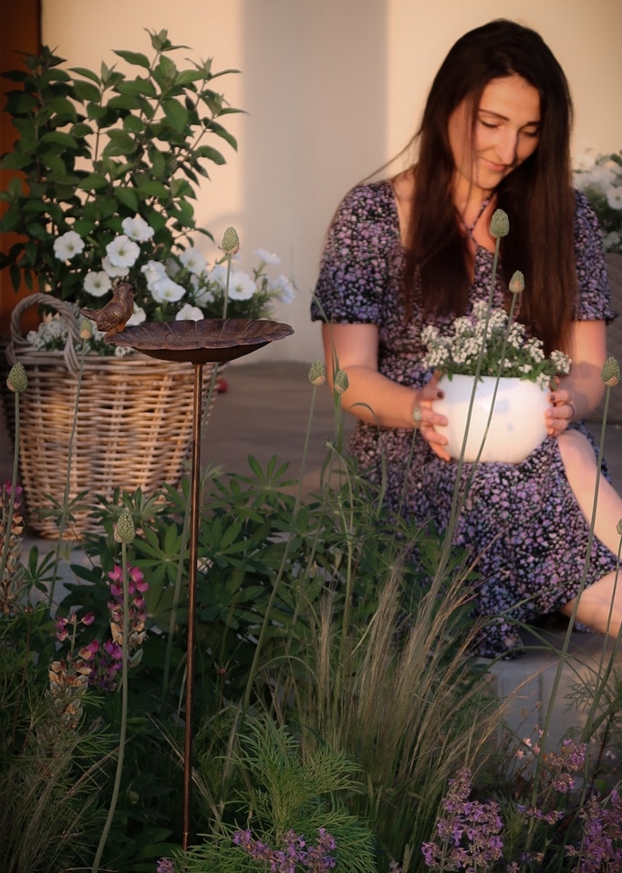 Decoratieve metalen vogelbad op standaard met vogel in tuin met bloemen en vrouw in jurk op achtergrond