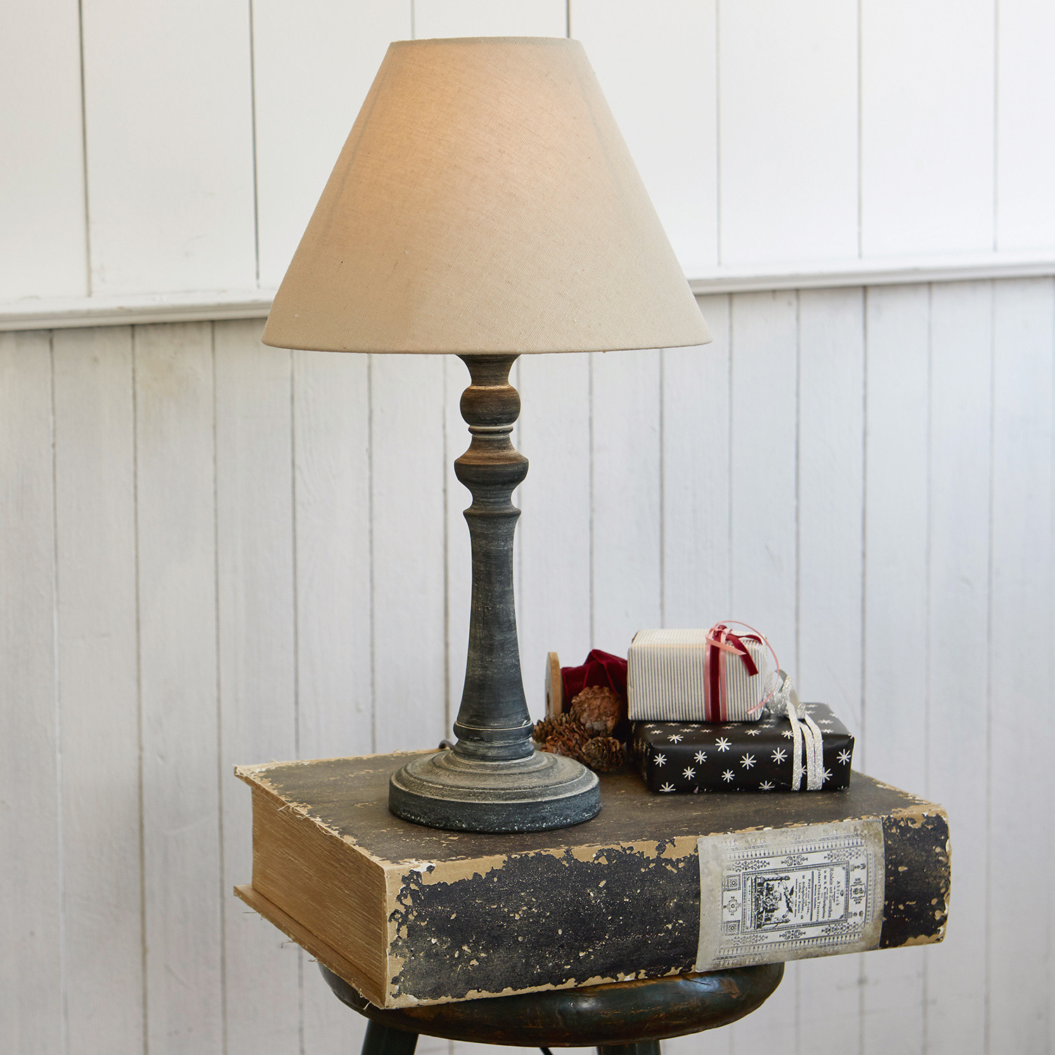 Tafellamp met beige kap en verouderde zwarte voet tegen witte muur