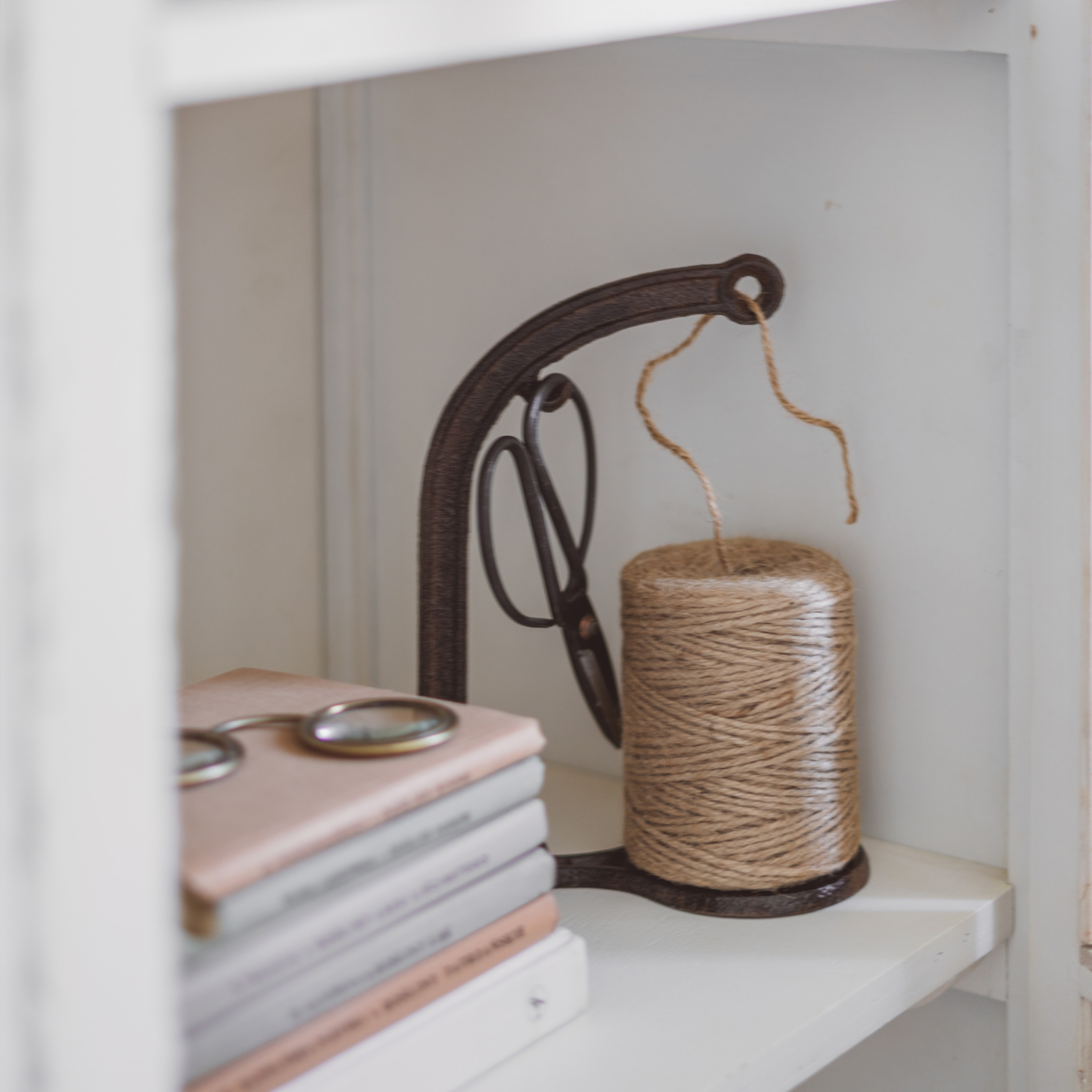 Metalen houder met beige garenrol en schaar op witte plank naast boeken