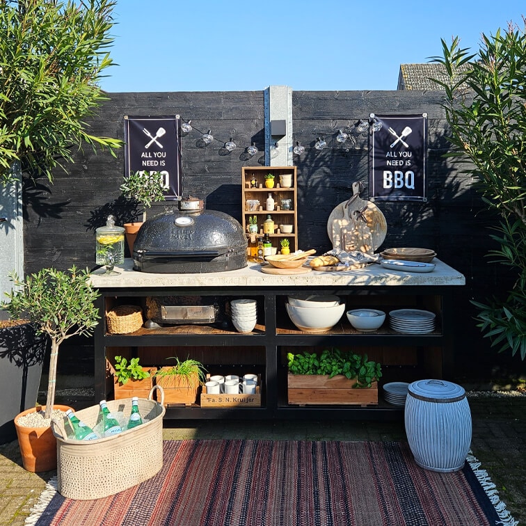 Buitenbarbecue met zwarte grill, wit werkblad, planten in potten en keukengerei