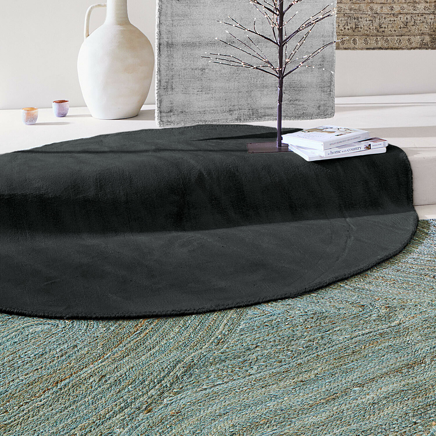 Ronde zwarte vloerkleed van zacht materiaal in lichte kamer met decoraties en boeken erop