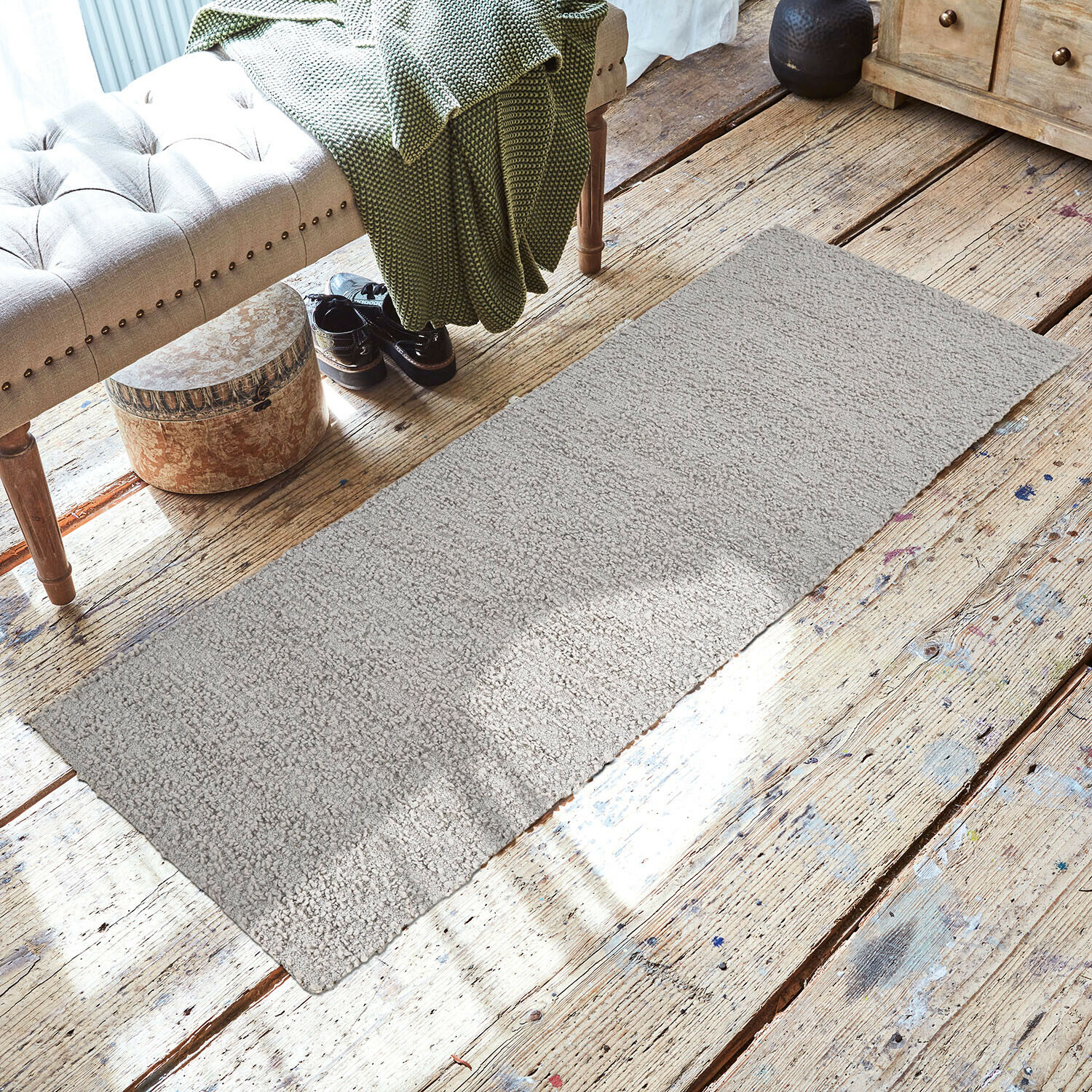 Grijs vloerkleed van zacht materiaal op houten vloer in gezellige ruimte met bank en groene deken