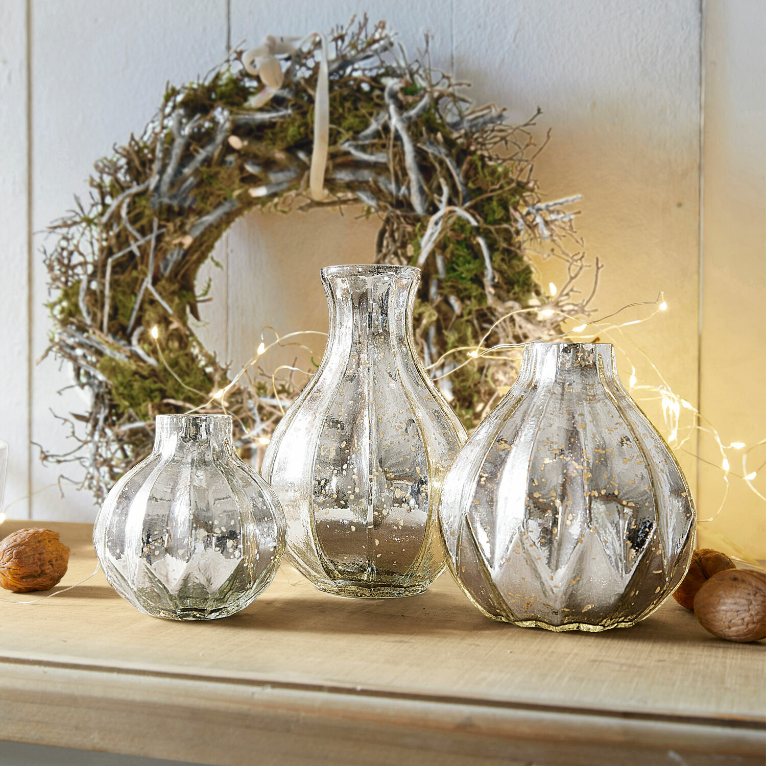 Vaas set van 3 Frido Set van drie decoratieve zilverkleurige glazen vazen op houten tafel met natuurlijke krans op de achtergrond