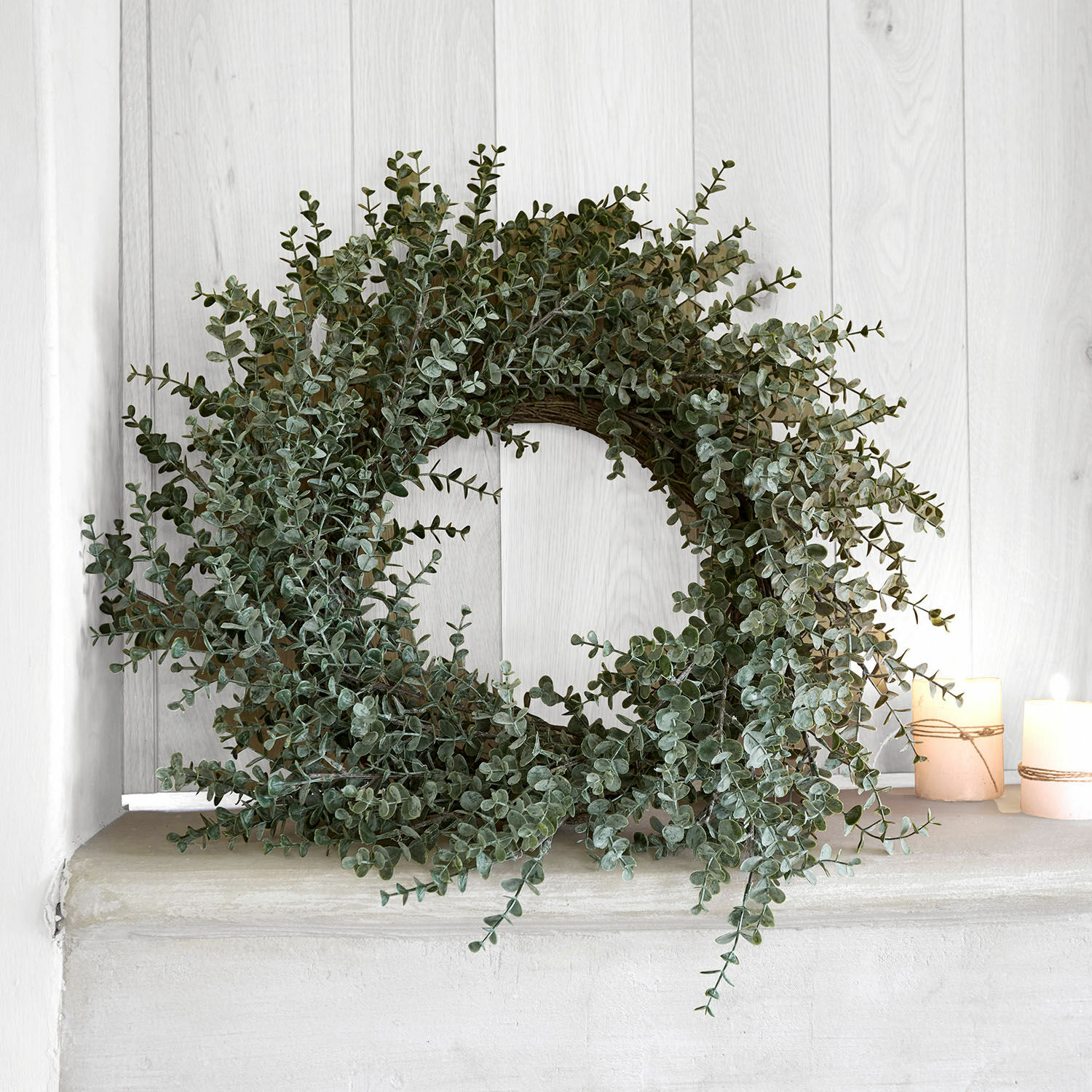 Decoratieve krans van groene eucalyptusbladeren op lichte plank met twee kaarsen