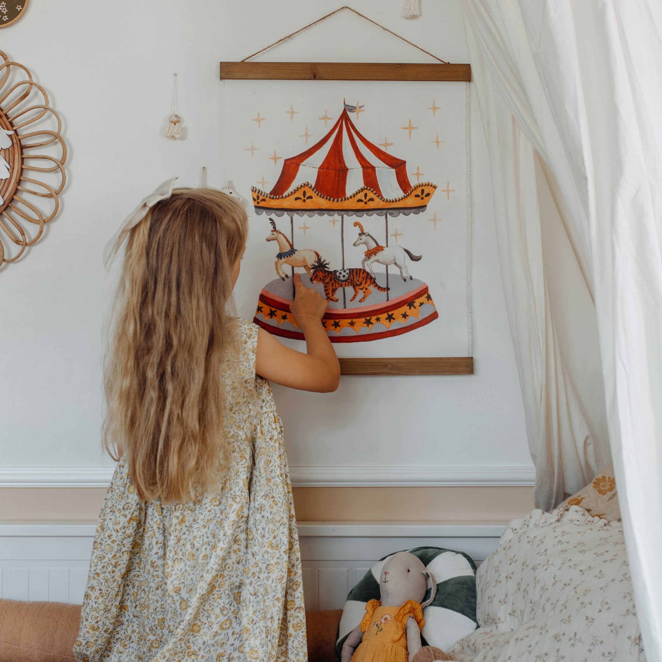 Meisje raakt afbeelding van carrousel met paarden aan in lichte kinderkamer met knuffel