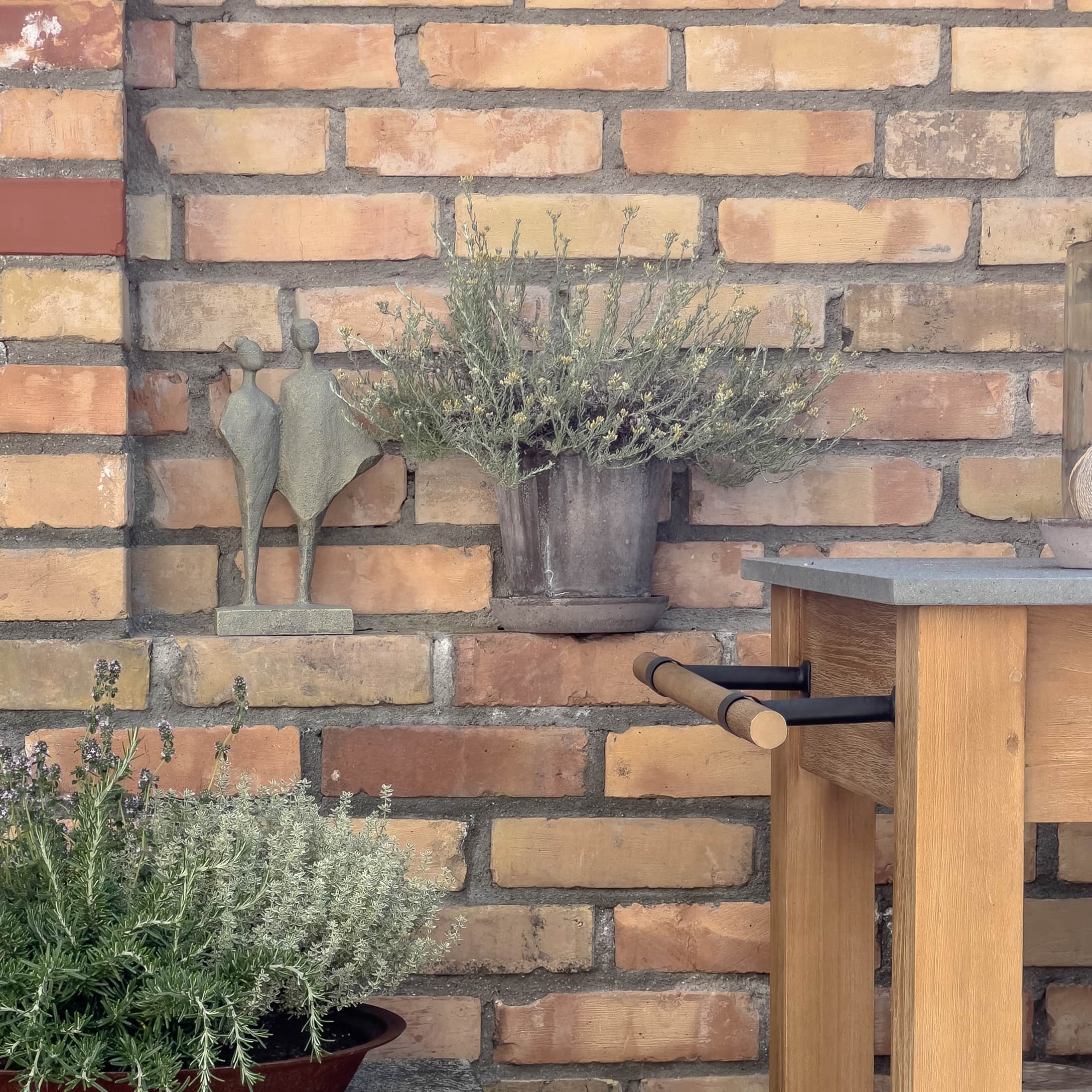 Decoratief beeld en bloempot met groene planten tegen een bakstenen muur en houten tafel