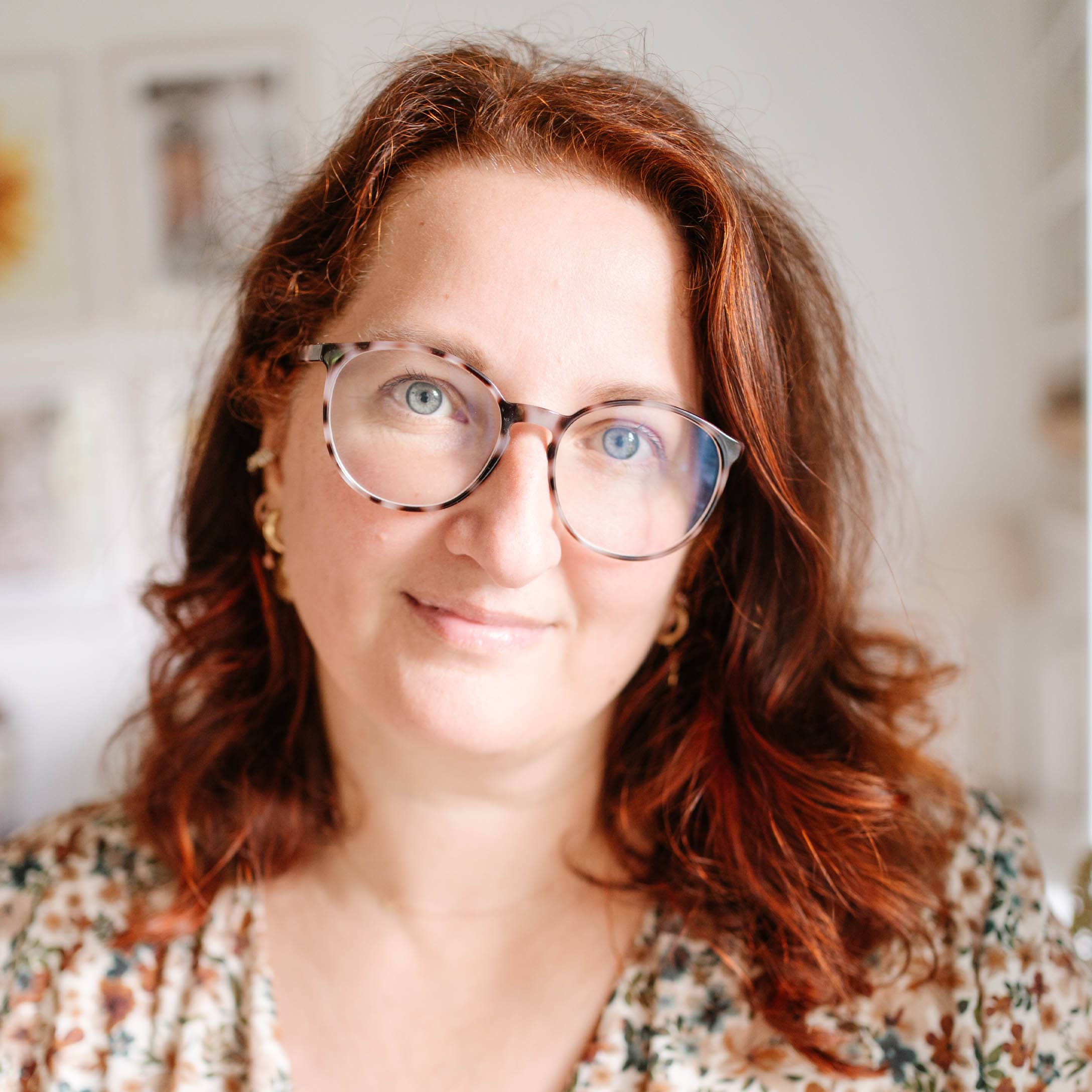 Portret van vrouw met rood haar en bril in bloemenblouse in lichte kamer