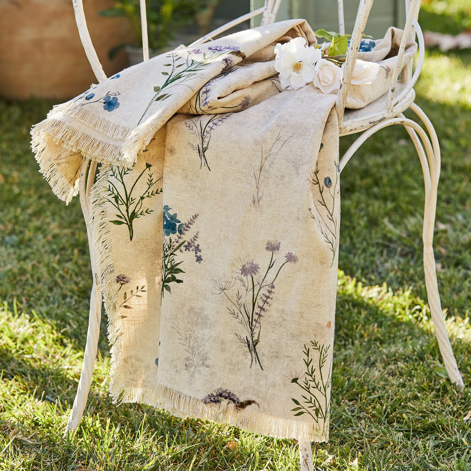 Plaid Cabinda Beige linnen tafelkleed met bloemenprint en franjes op witte metalen stoel in tuin