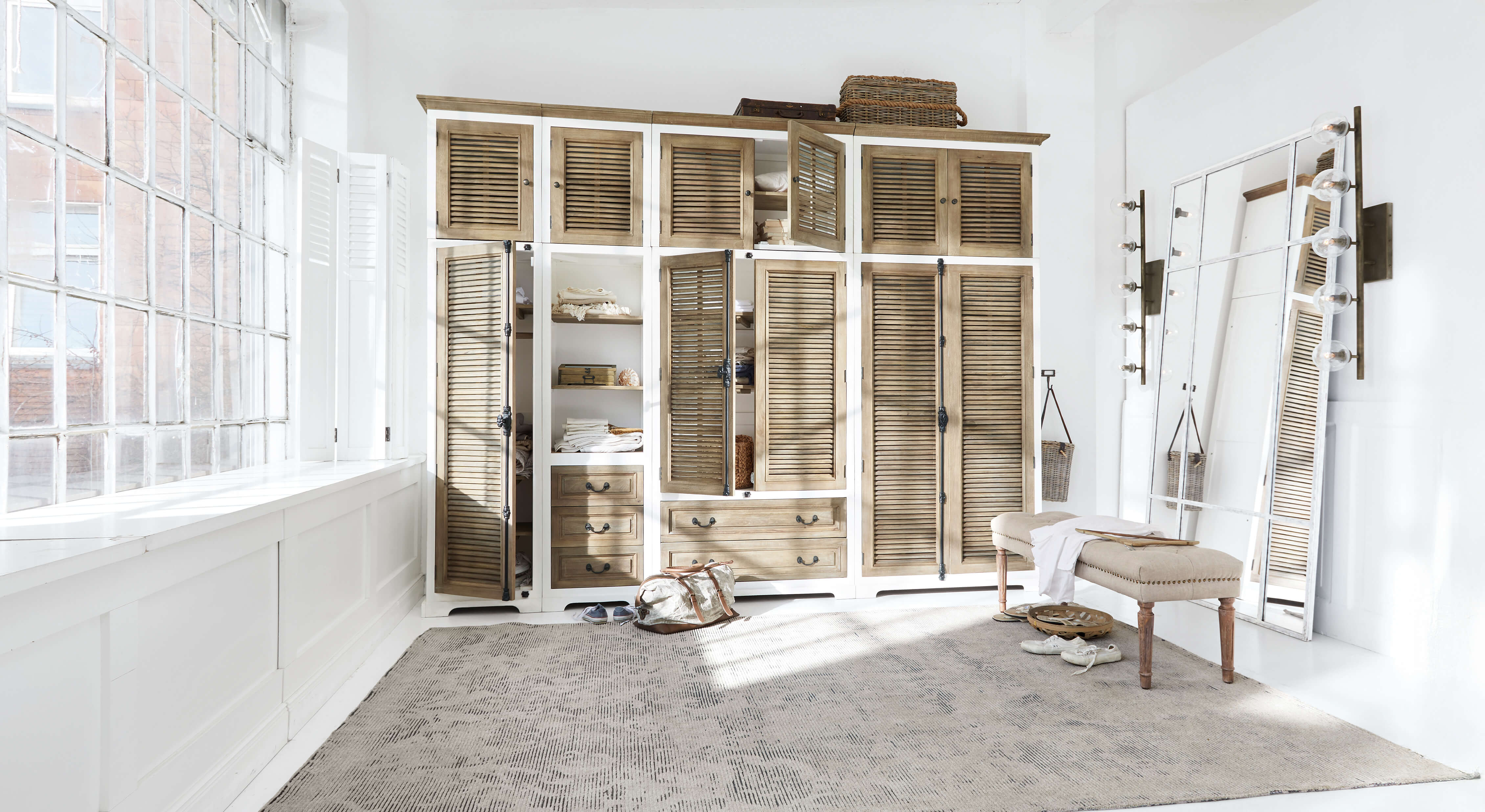 Ruime kast van wit en natuurlijk hout met lamellen deuren en grote spiegel in lichte kamer