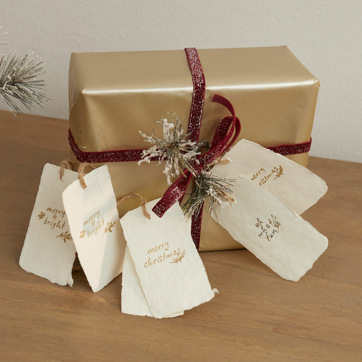 Hanger set van 6 Aamira Gouden cadeau met bordeaux lint en witte papieren kerstlabels op houten tafel