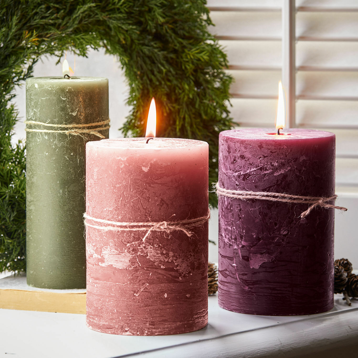 Drie rustieke kaarsen van was in groen, roze en bordeaux met decoratief juten touw